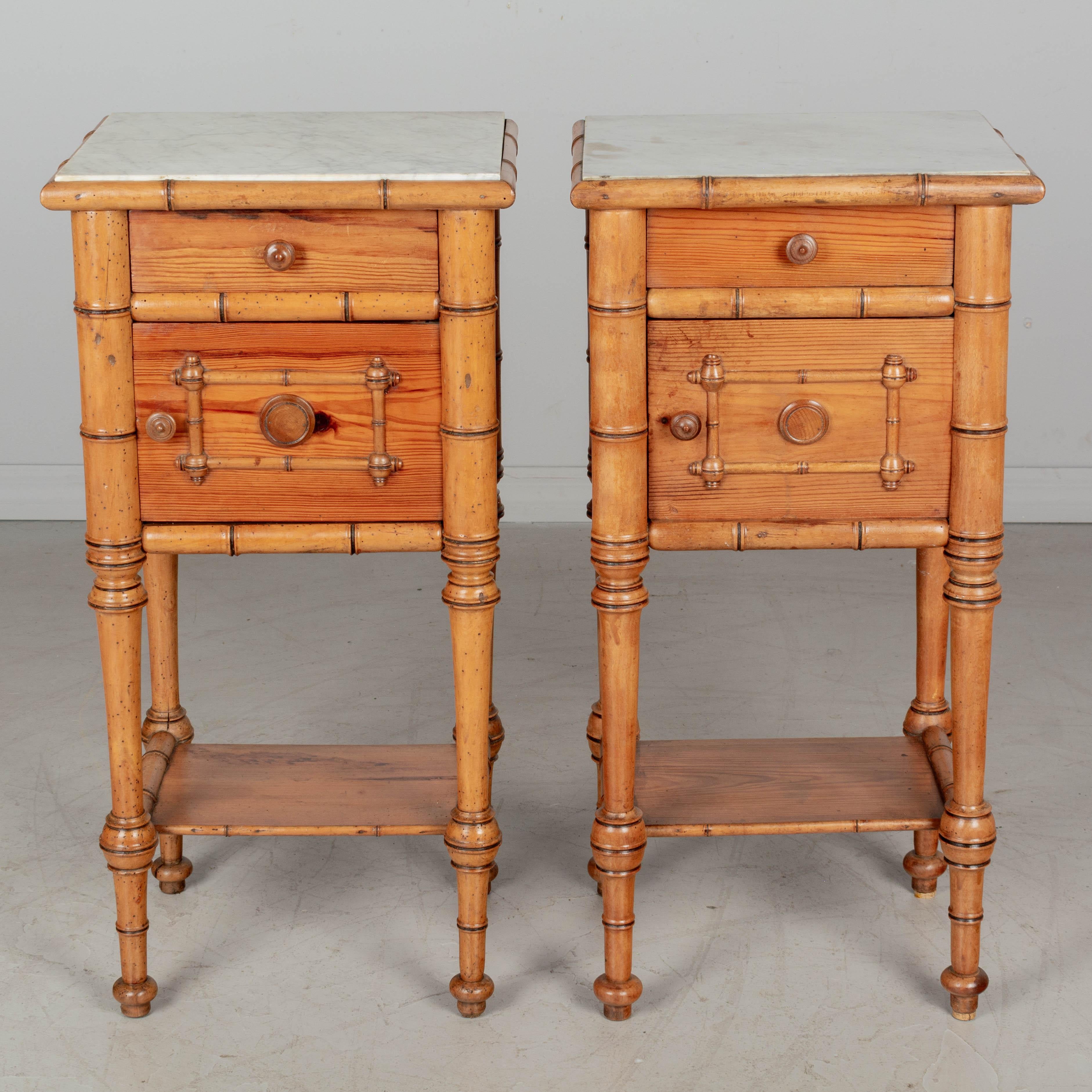 A pair of 19th century French faux bamboo marble top bedside tables, or nightstands, made of pine and turned beechwood. Dovetailed drawer above a cabinet door and lower shelf. Sturdy turned legs. Inset white marble top. Circa 1880-1900. 
Dimensions: