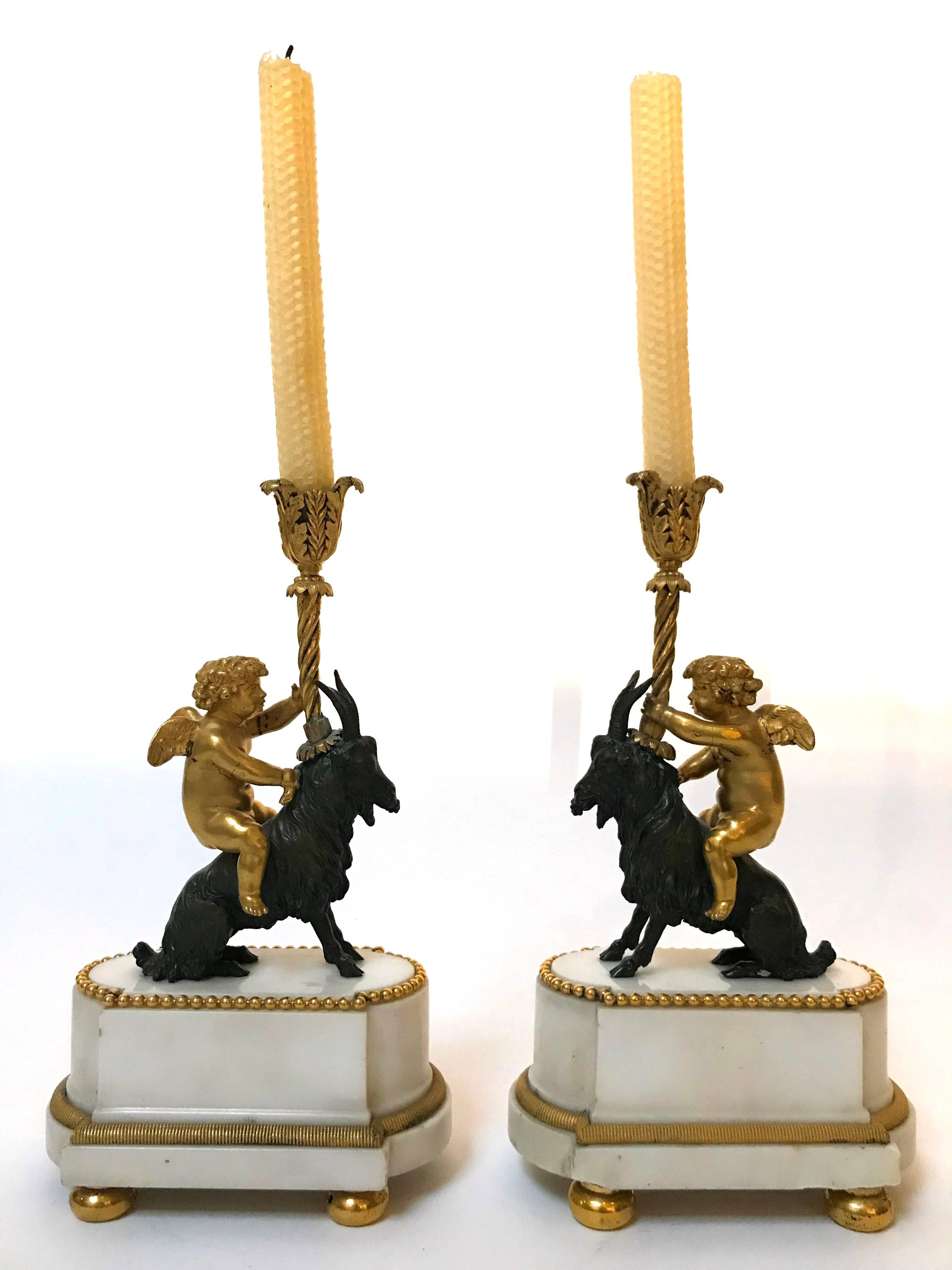 A charming pair of French Napoleon III white marble, bronze and gilt bronze torcheres depicting cherubim atop goats holding a single bobeche for a candle.
