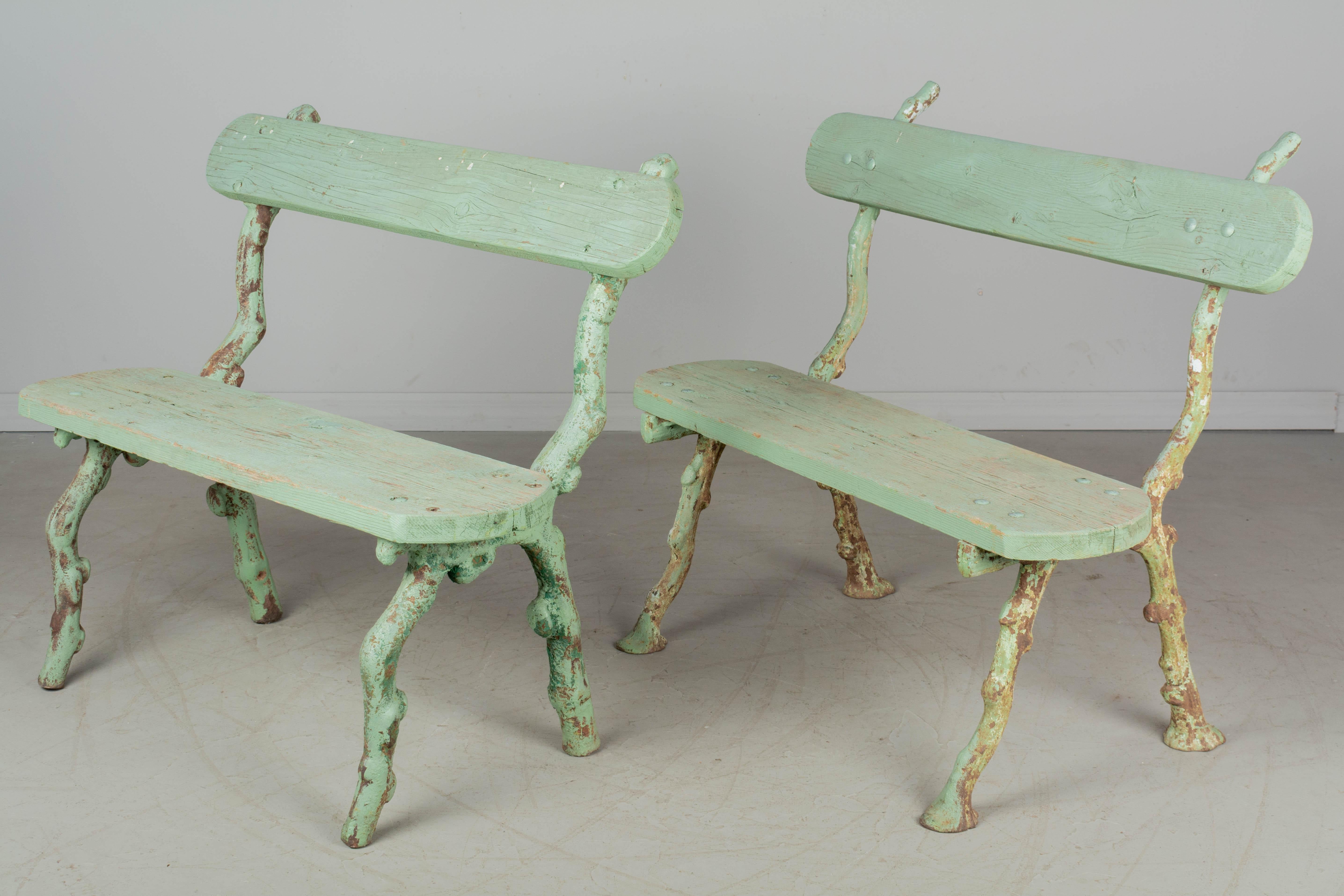 A pair of similar 19th century French garden benches, each with cast iron faux bois frame and oak board seat and backrest. Old pale green painted patina. Nice quality iron work and good sturdy condition. Circa 1870-1890. 
Dimensions: 39
