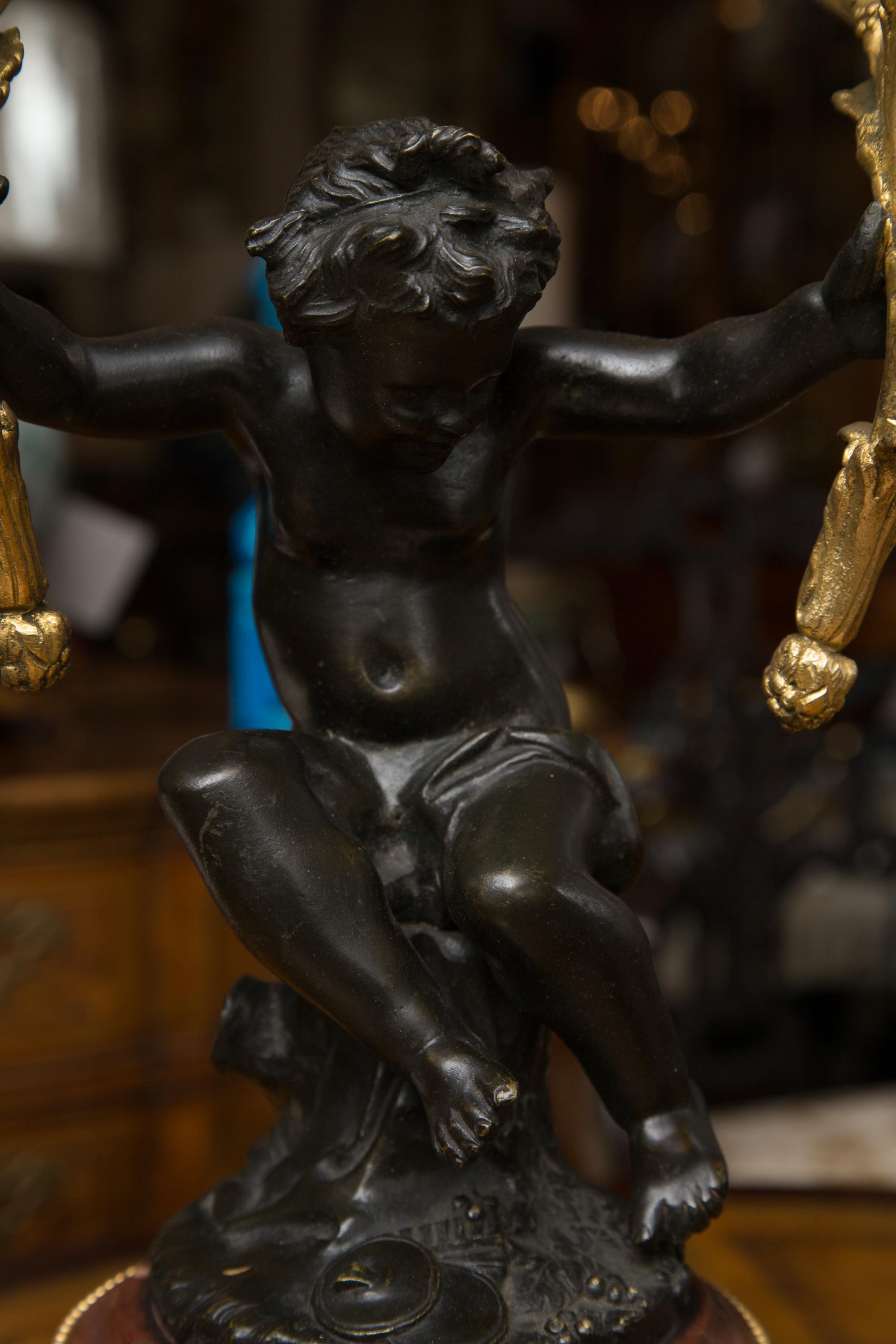 These are impressive pair of 19th century gilt metal candelabra held by an exquisitely patinated bronze cherubs'. They are placed on rouge marble and decorated circular bases decorated also with gilt metal accents. The black plinths add a depth to