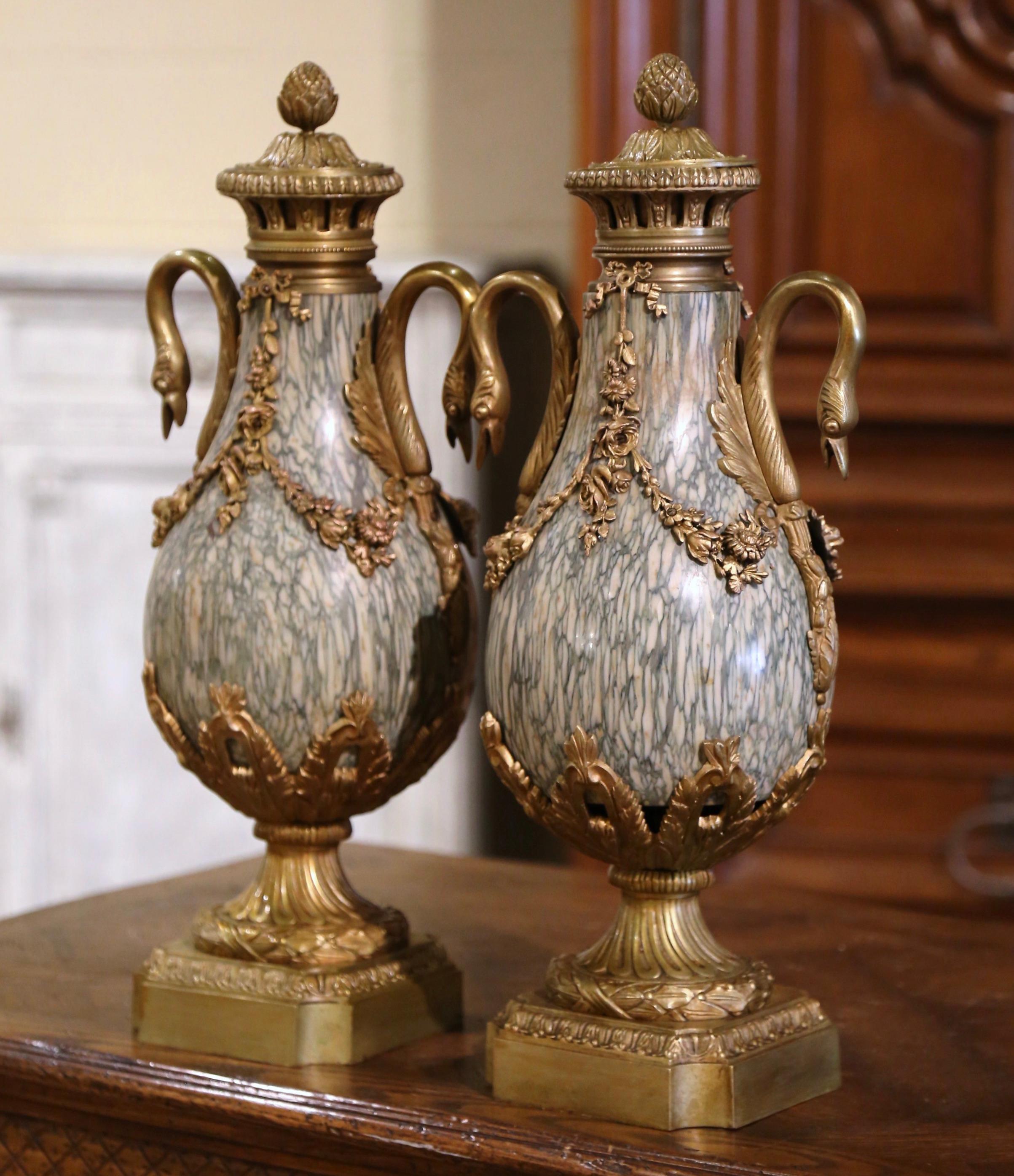 Decorate a mantel or buffet with this colorful pair of antique urns. Crafted in France, circa 1870, each vessel stands on a square bronze base decorated with concave corner. Each cassolette is dressed with a lid embellished with decorative