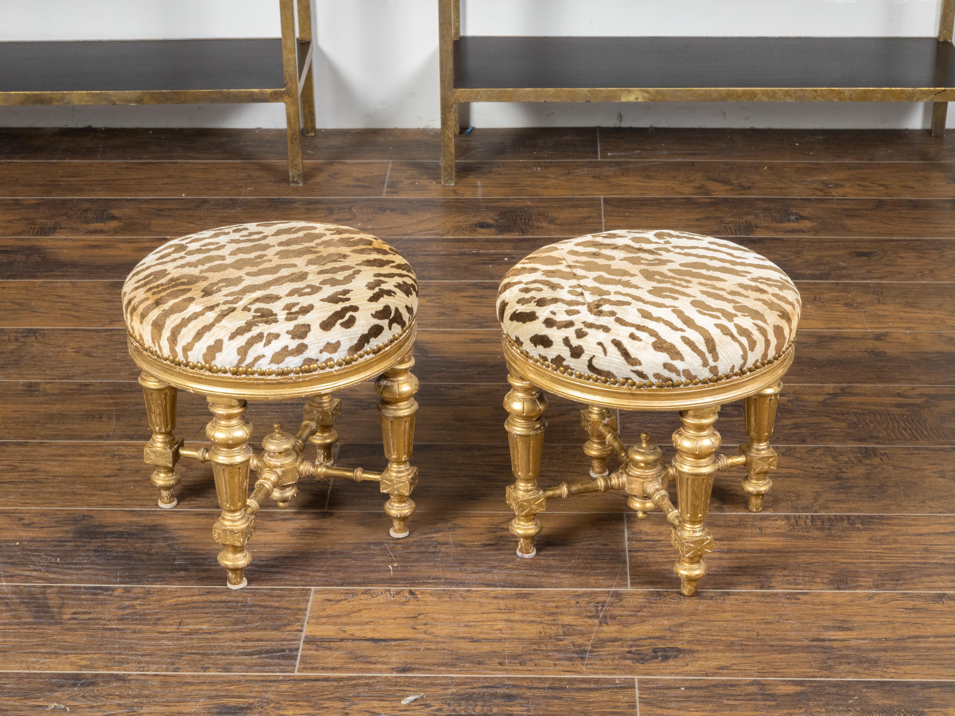 Une paire de tabourets en bois doré français du 19ème siècle, avec des pieds cannelés, des traverses et une tapisserie de style léopard. Créée en France au XIXe siècle, cette paire de tabourets en bois doré présente une assise circulaire recouverte
