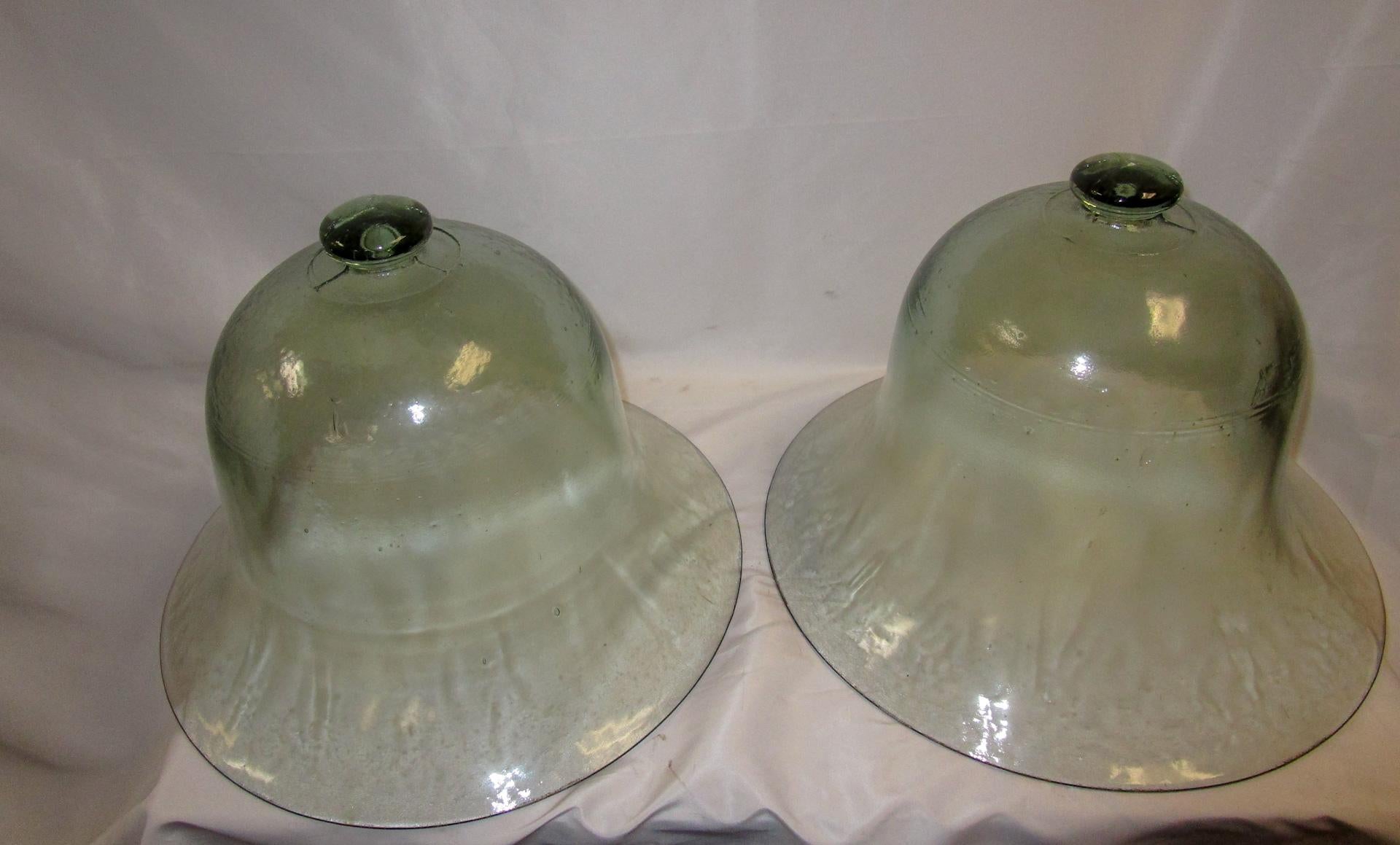 The French developed the glass cloche, or bell jar as a way to protect early garden plants from bleak cold and frost-a hothouse in miniature. This pair of hand blown thick glass large 19th century French bell shaped garden cloche are formed as a