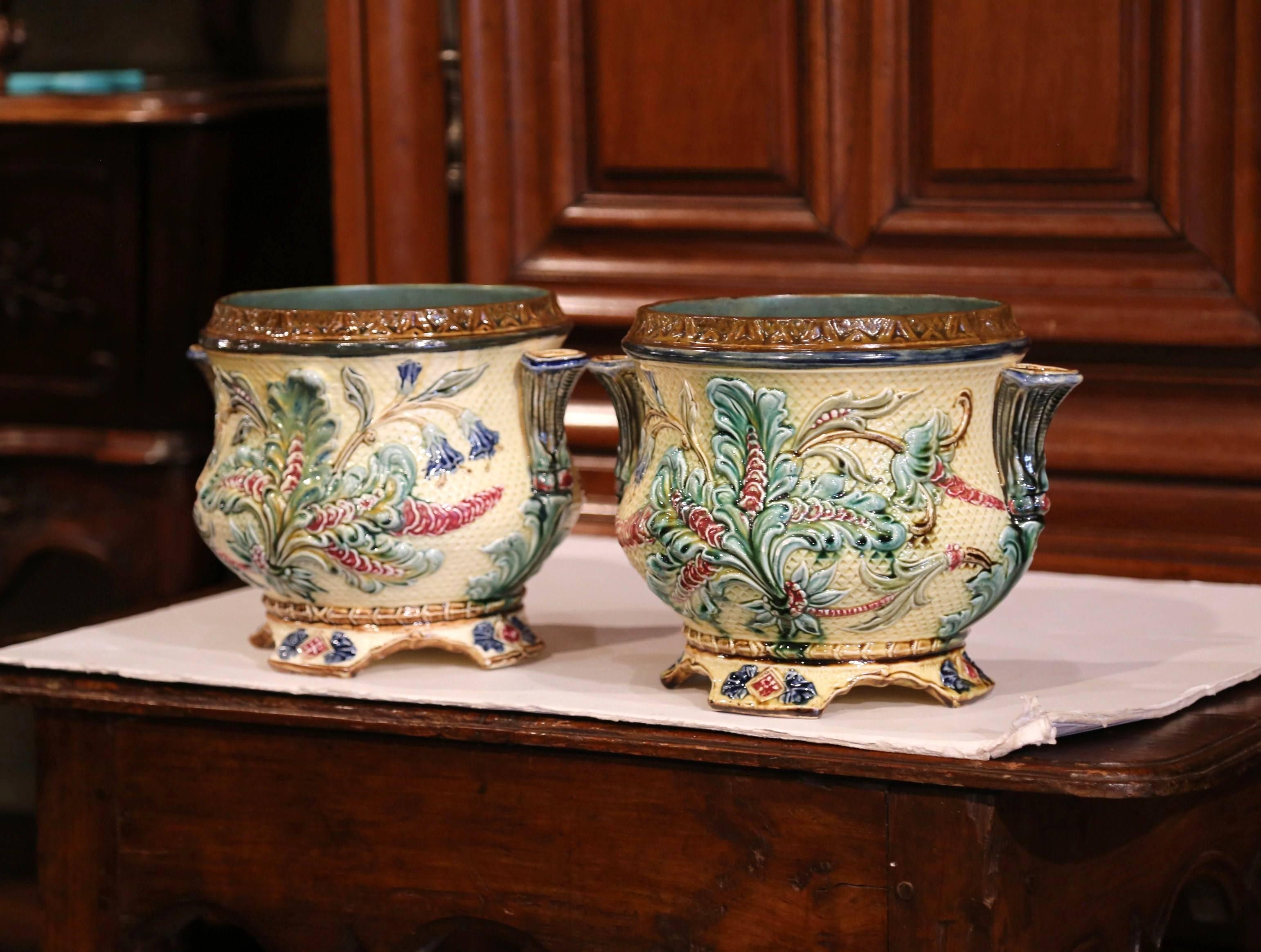 Decorate your mantel with this nice pair of hand-painted, Majolica planters from France, circa 1880. Both antique vases have flower shaped handles on the sides, and feature colorful leaves and floral motifs in a beige, green and pink palette and