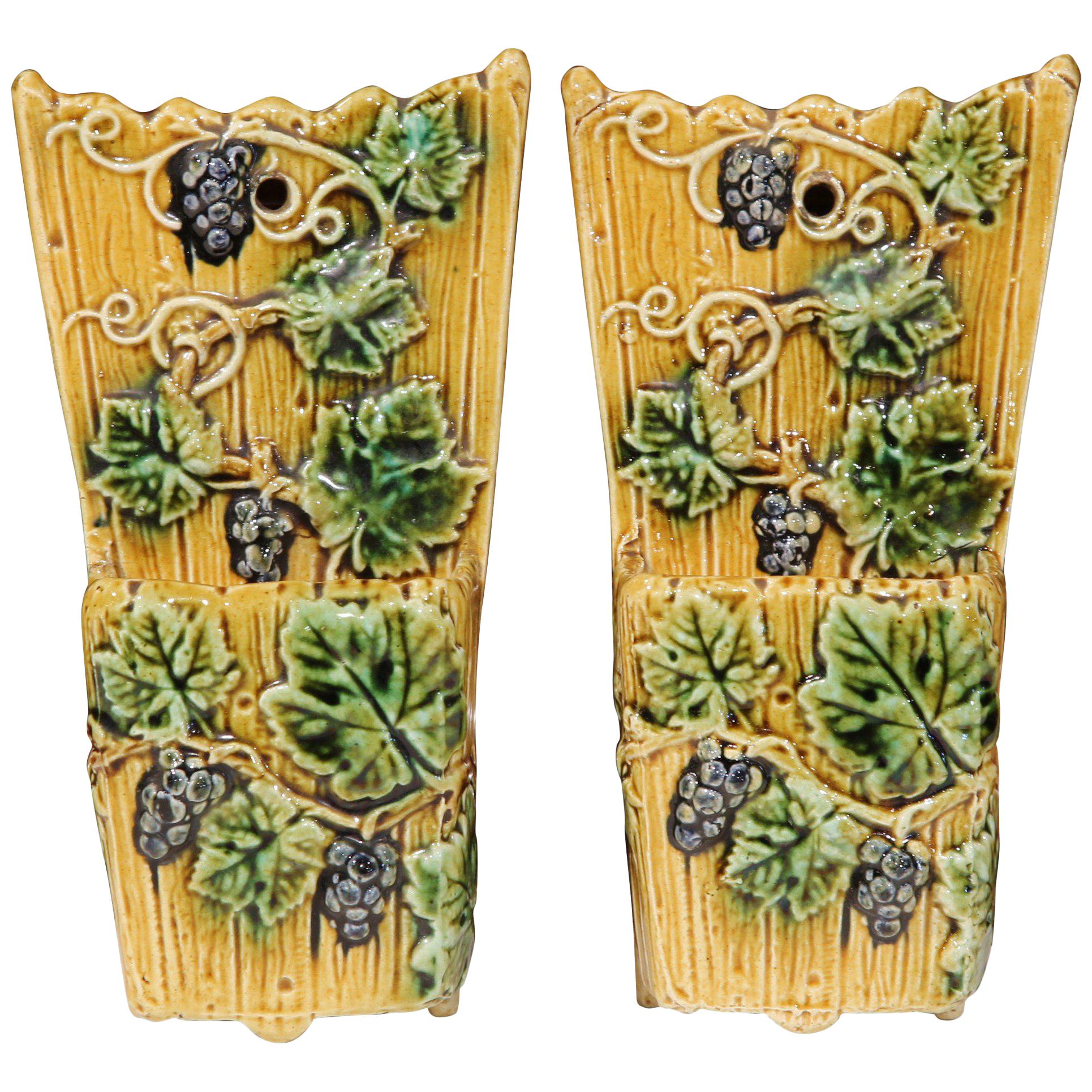 Hang plants or other greenery on the wall using this fine, colorful pair of antique Majolica wall pots. Created in France, circa 1890, the wall hanging vases feature grapes and vines motifs in high relief in a vivid green and yellow color palette.