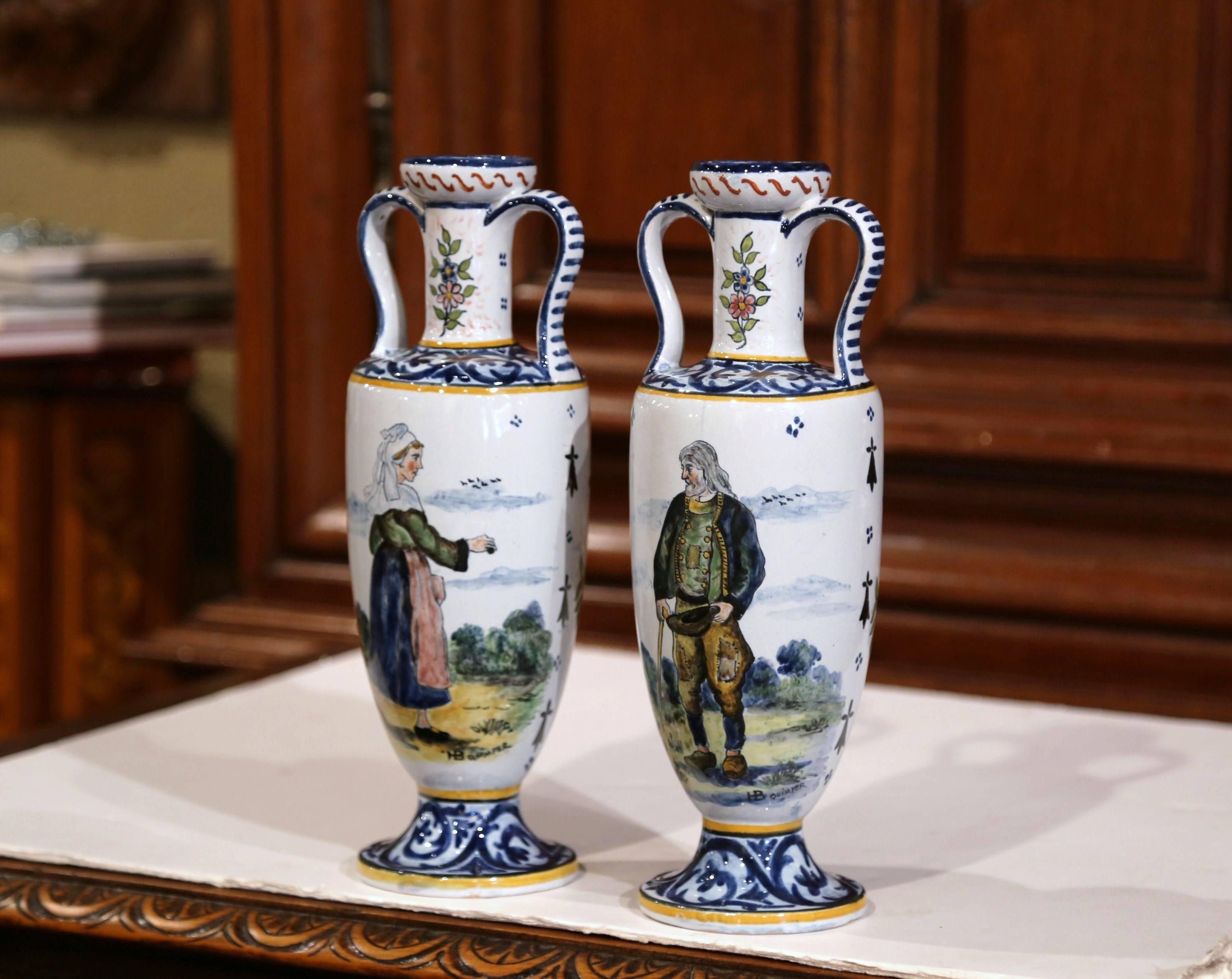 Decorate a mantel or table with this colorful pair of antique faience vases. Crafted in Brittany, France, circa 1880, both hand-painted vases with side handles show Britons people dressed in traditional outfits on one side, and flower bouquet on the