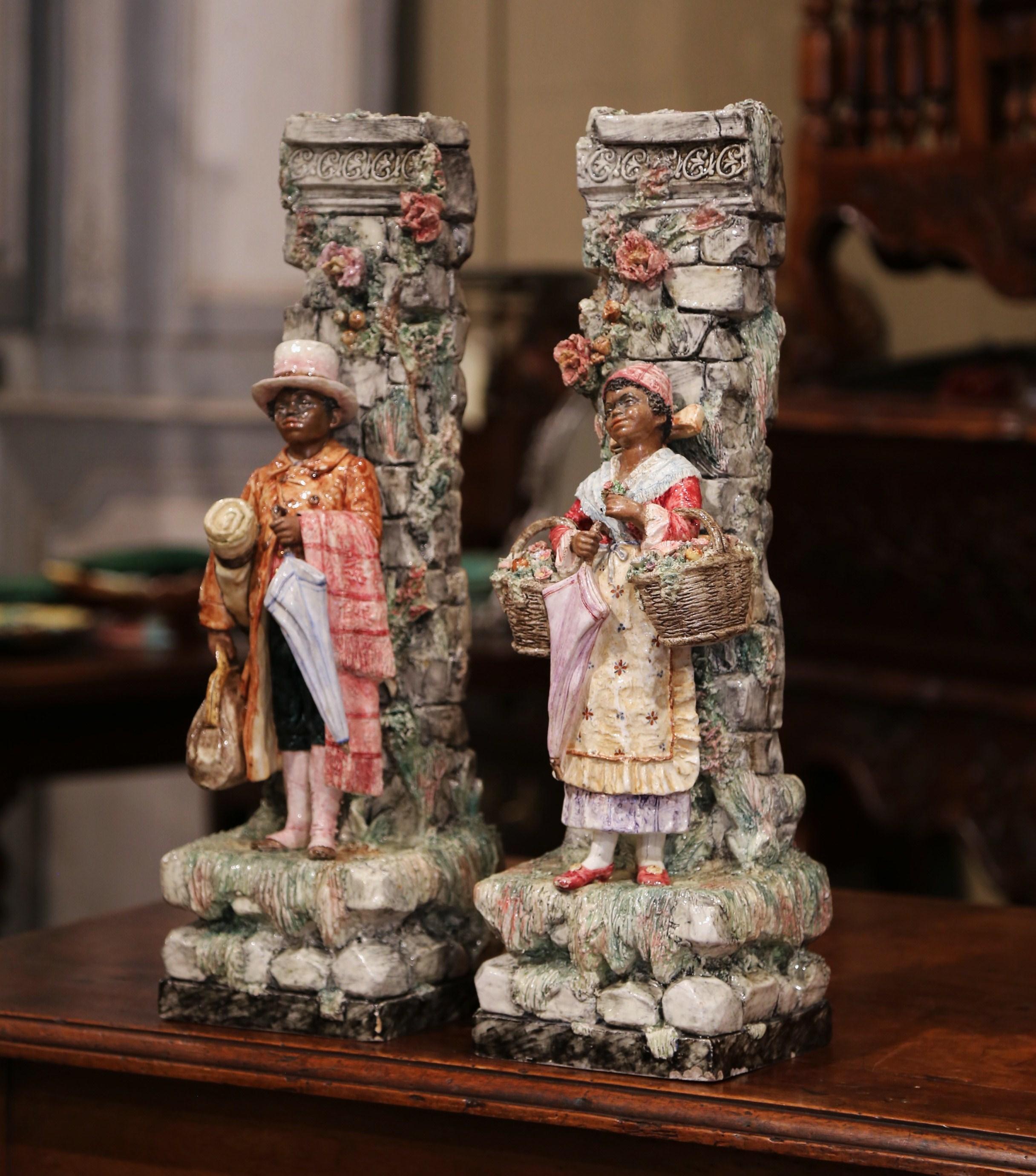 Place this large and unique pair of antique Majolica vases on a console or shelf. Crafted in France, circa 1880, the colorful ceramic planters are tall and thin and feature two figures in high relief and standing in front of a carved stone wall.