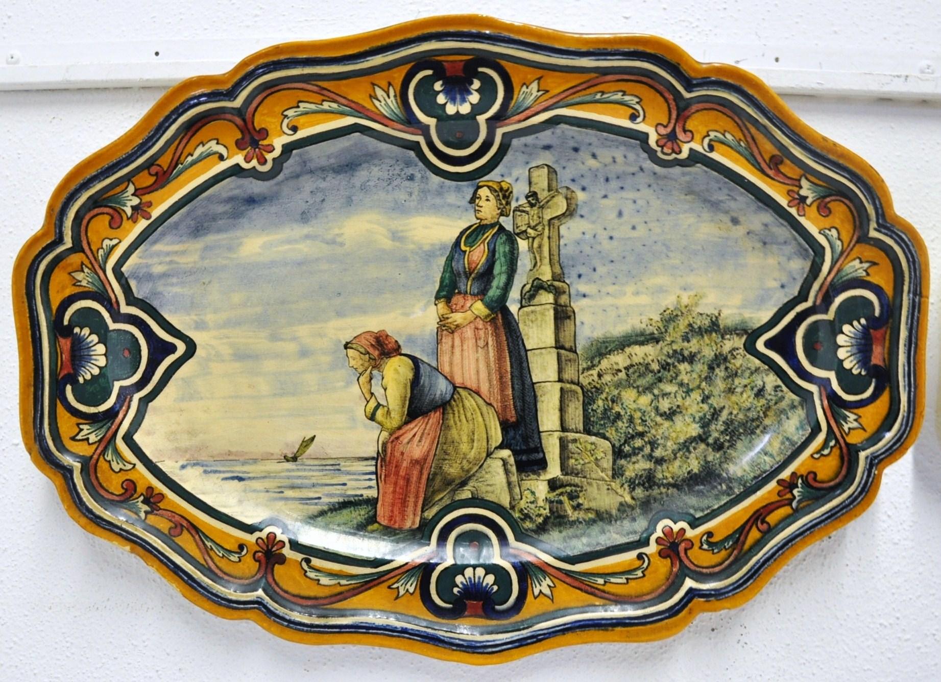 These charming hand painted plates were sculpted in the Faiencerie de Nevers, France, circa 1850. The antique ceramic platters depict two figural scenes; an interior, domestic scene with a man and a woman seated by a fire, and two women praying in