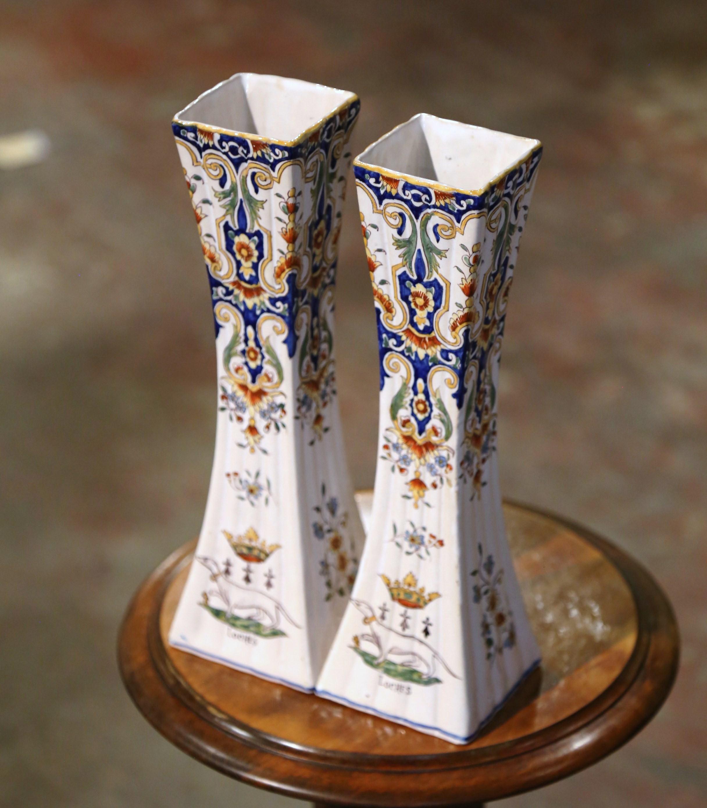 Incorporate beautiful colors into your home with this elegant pair of antique ceramic trumpet vases. Crafted In Normandy circa 1899, each vessel is ornate in decoration yet simple in shape; the tall, colorful vase features a square bottom and a wide