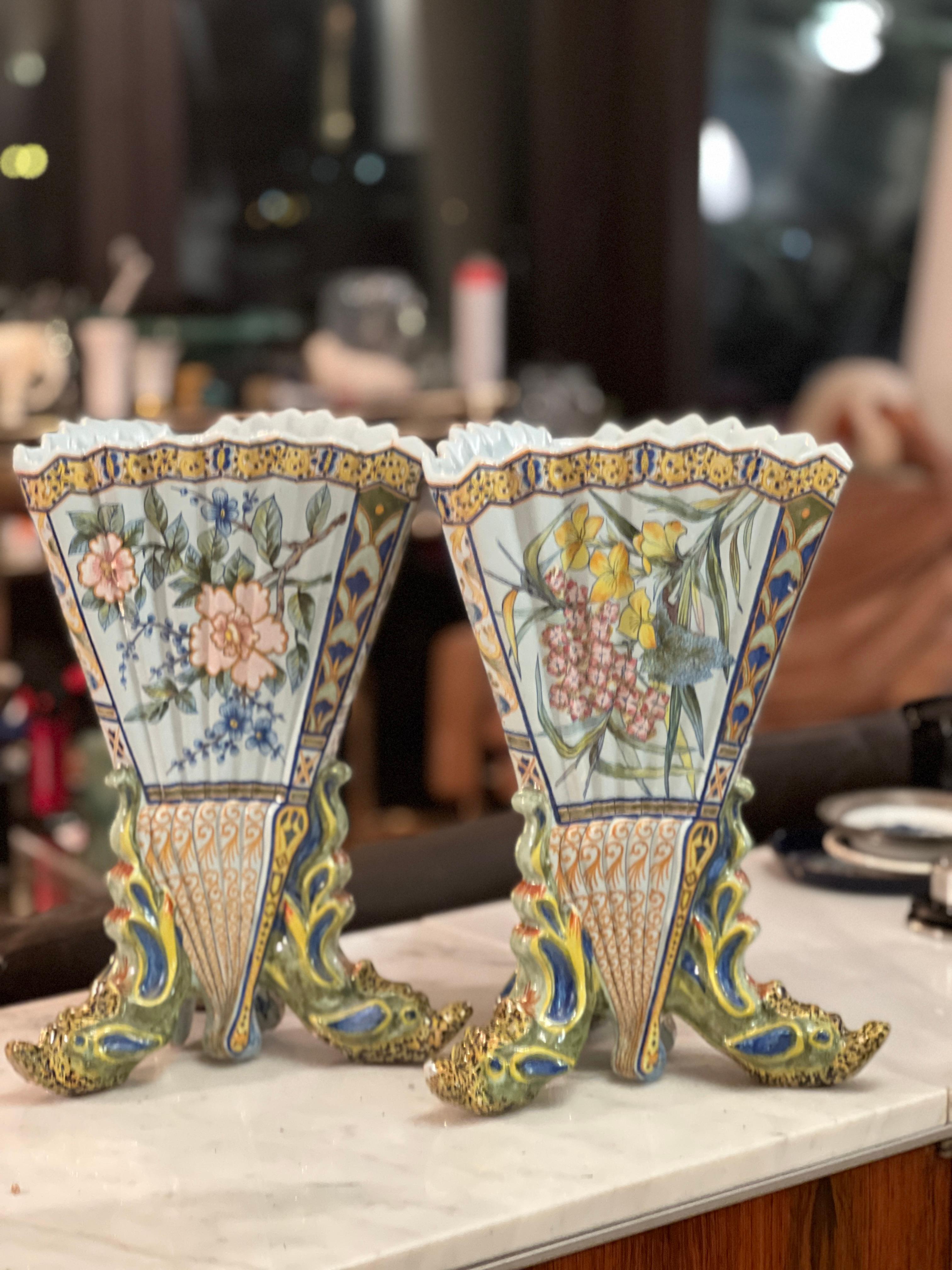 Stunning pair of large antique vessel. Created in Brittany, France in the late 19th century. The colourful hand painted ceramic vase stands on three head shaped feet, over a triangular and tapered form with scalloped rim and accordion shaped panels.