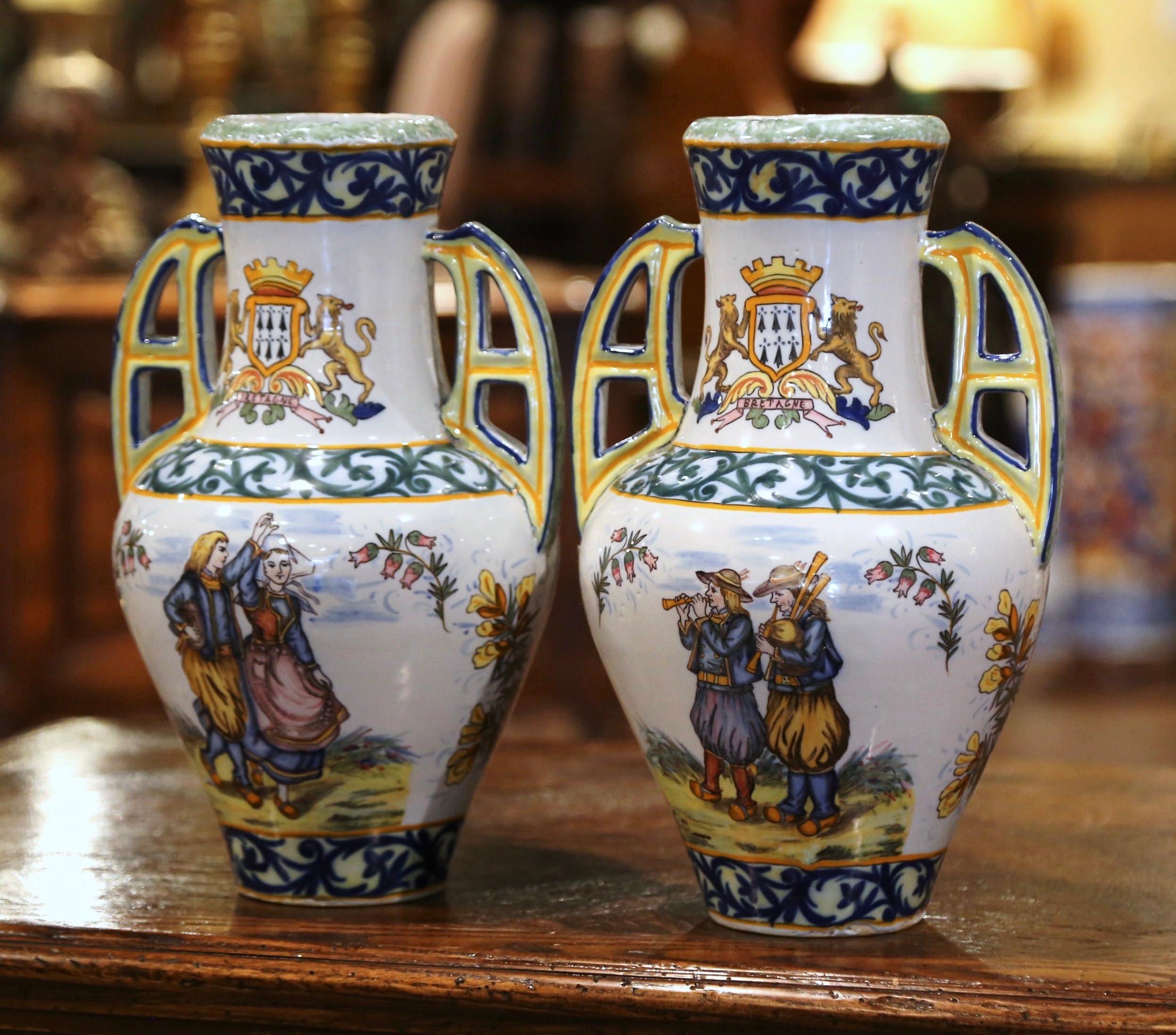 Decorate a mantel or table with this colorful pair of antique faience vases. Crafted in Brittany, France, circa 1890, both hand painted vases with side handles show Britons people dressed in traditional outfits on one side, and the Brittany coat of