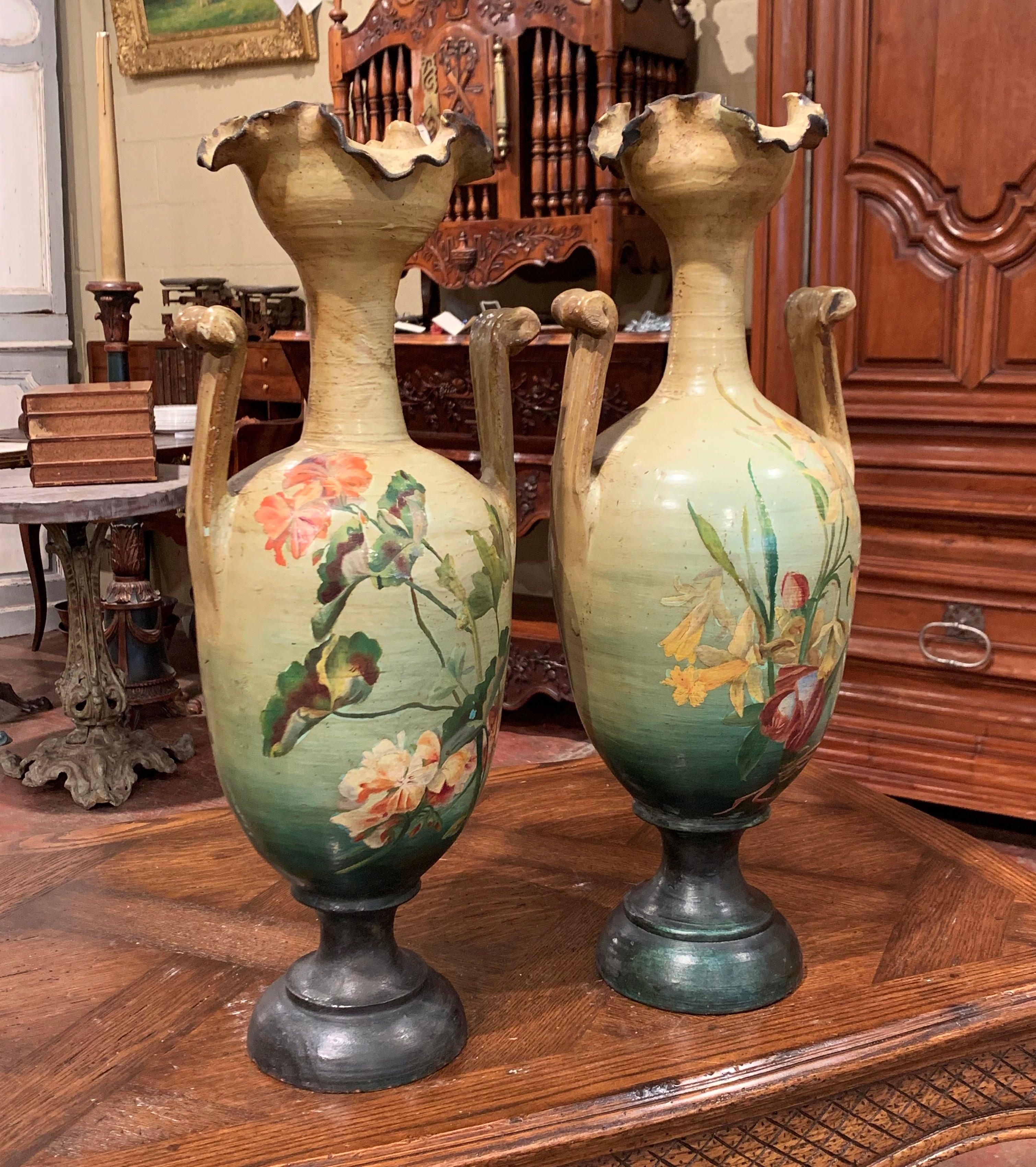 Sculpted from terracotta, these large vases were created in southern France circa 1900. Each painted, sculptural vessel sits on a round, dark green base, and feature handles on both side. Each vase has tall neck, wide mouth and an artful,