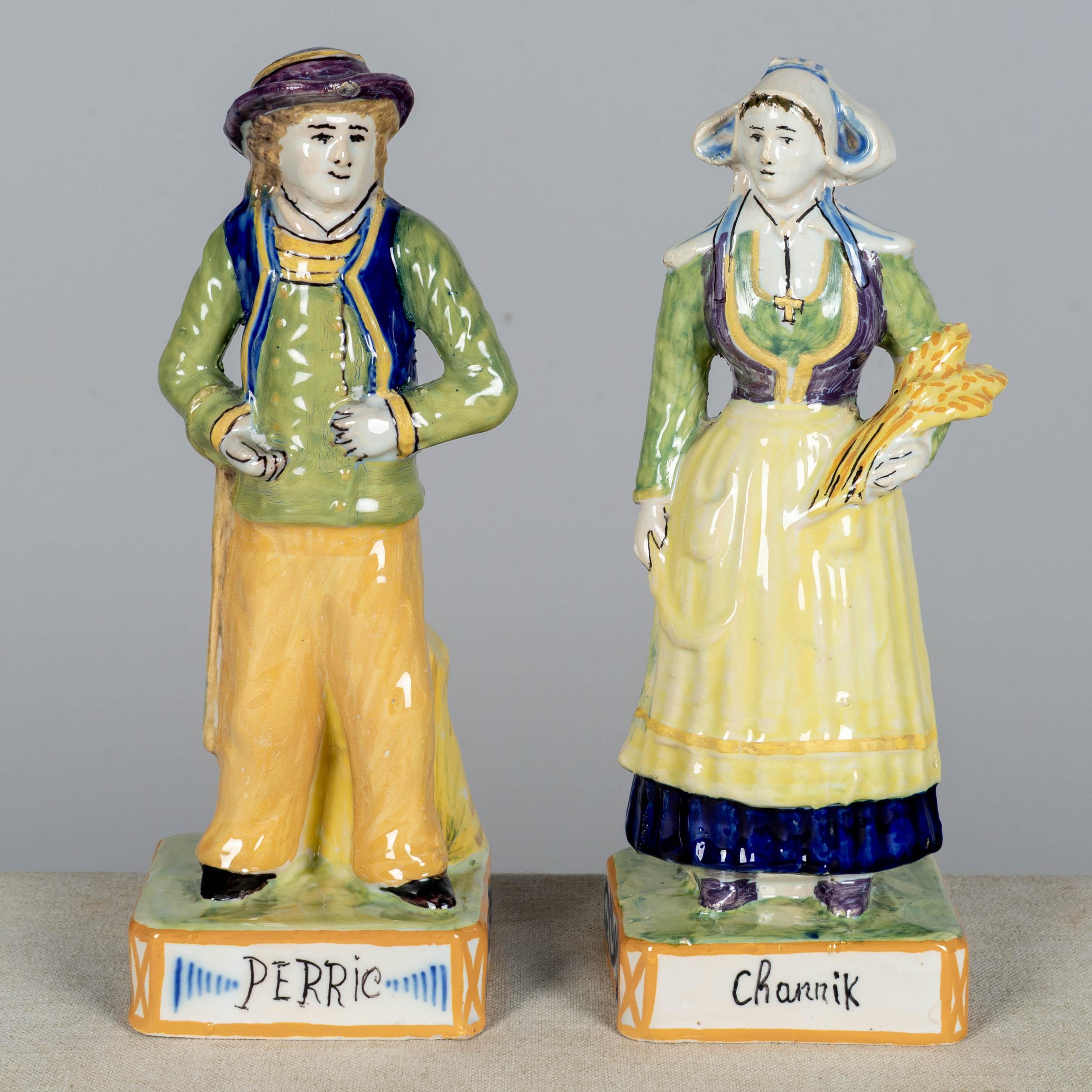 A pair of late 19th century French Henriot Quimper faience statues, or figurines, of Perric and Channik. Polychrome enameled earthenware, hand-painted in yellow, green, blue and purple. These Breton figurines are part of a tradition of portraying