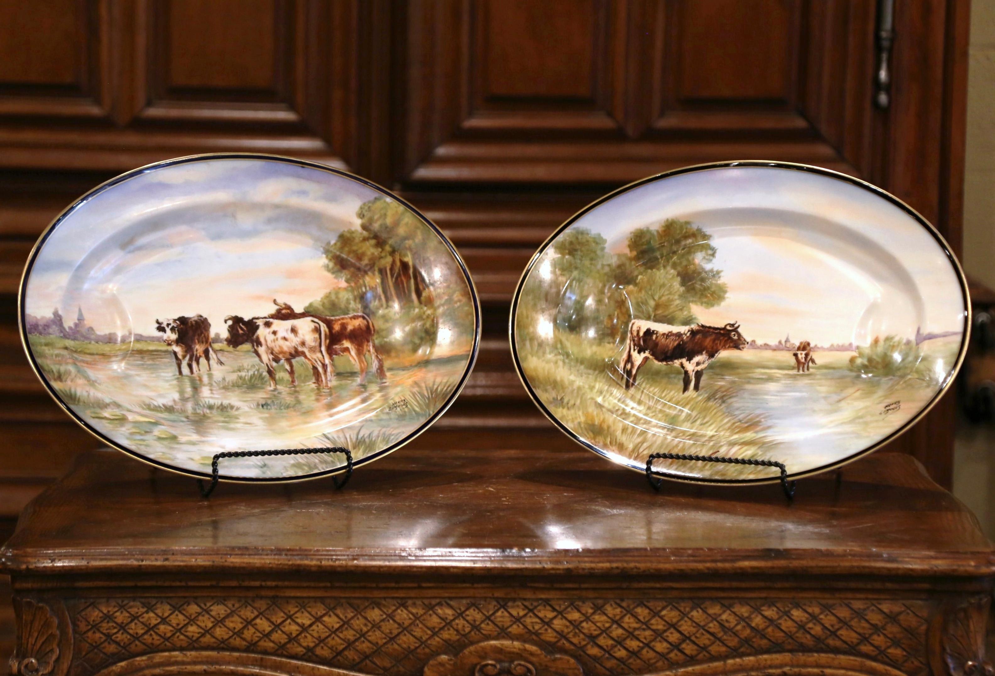 Decorate a wall or a shelf with this large and colorful pair of antique platters. Crafted in Limoges France by Haviland circa 1880 and signed, each hand painted porcelain plate is oval in shape, and features a pastoral scene with cows in a pasture.