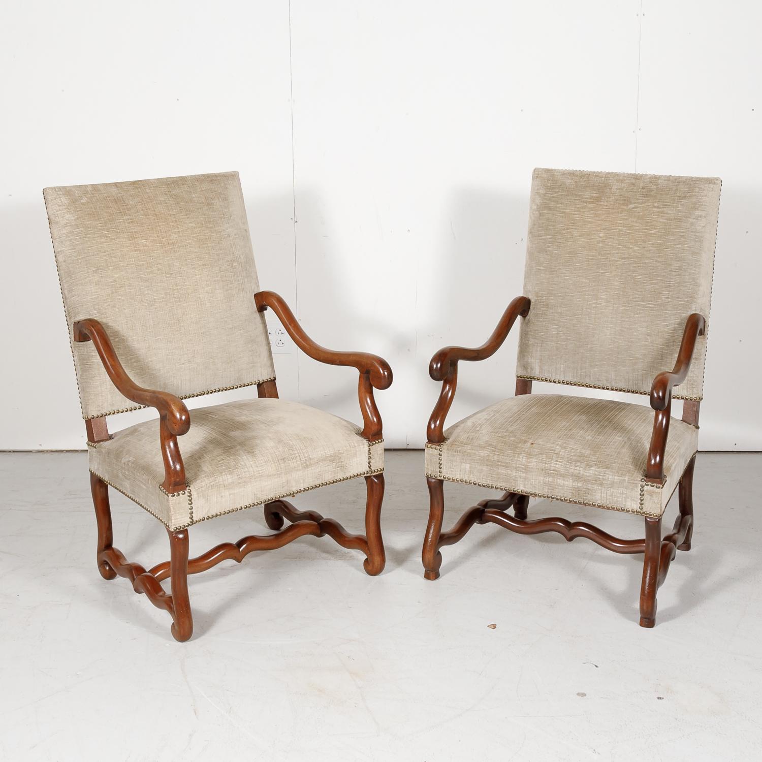 Lovely pair of 19th century French Louis XIII style os de mouton armchairs, circa 1880s. Handcrafted of sold walnut in Lyon, these oversized fireside armchairs have beautifully carved walnut frames with tall rectangular backs and gently scrolling