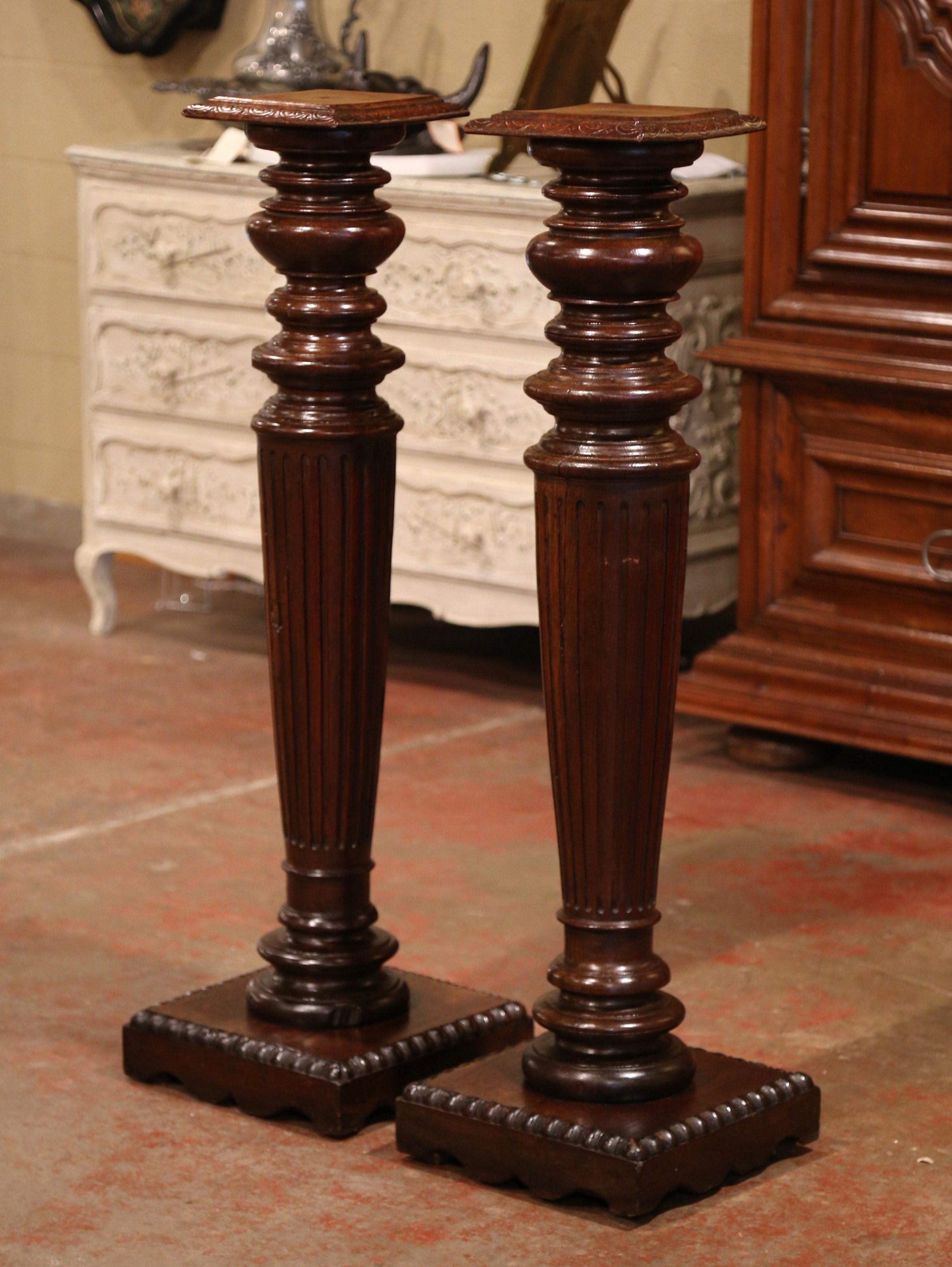 These elegant antique pedestals were crafted in Normandy, northern France, circa 1870. Standing on a wide square plinth base, each tall oak column has a long tapered and turned stem and features a square swivel top surface decorated with carved