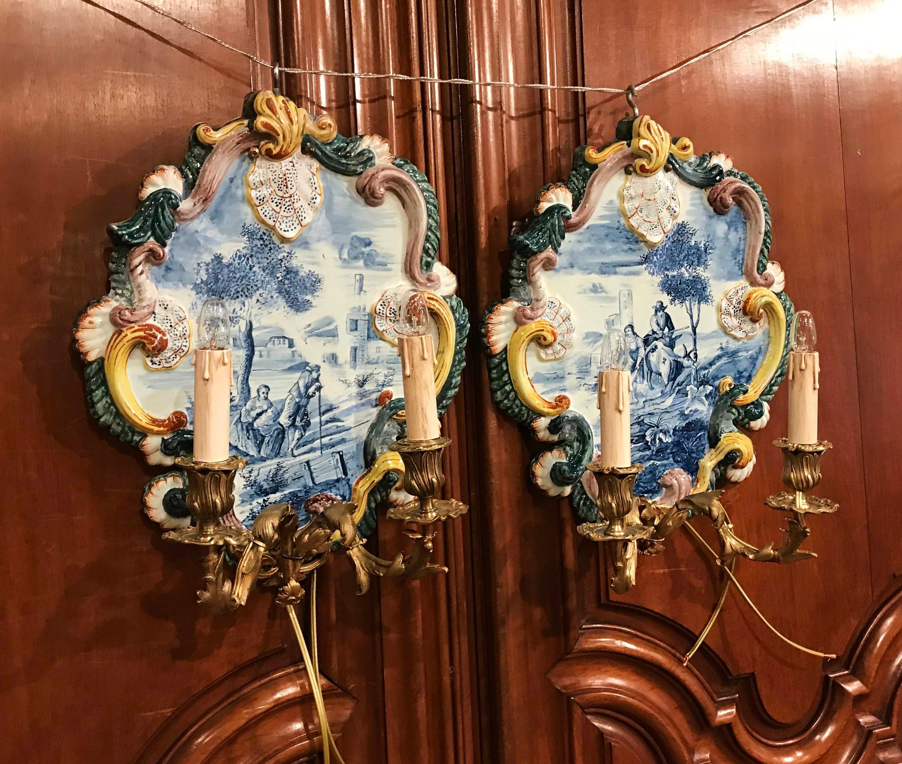 Decorate a living room or dining room with this colorful pair of antique wall sconces. Crafted in France circa 1820, each Louis XV style light fixture is decorated with two bronze scroll arms with leaf decor. The base of each sconce is a colorful