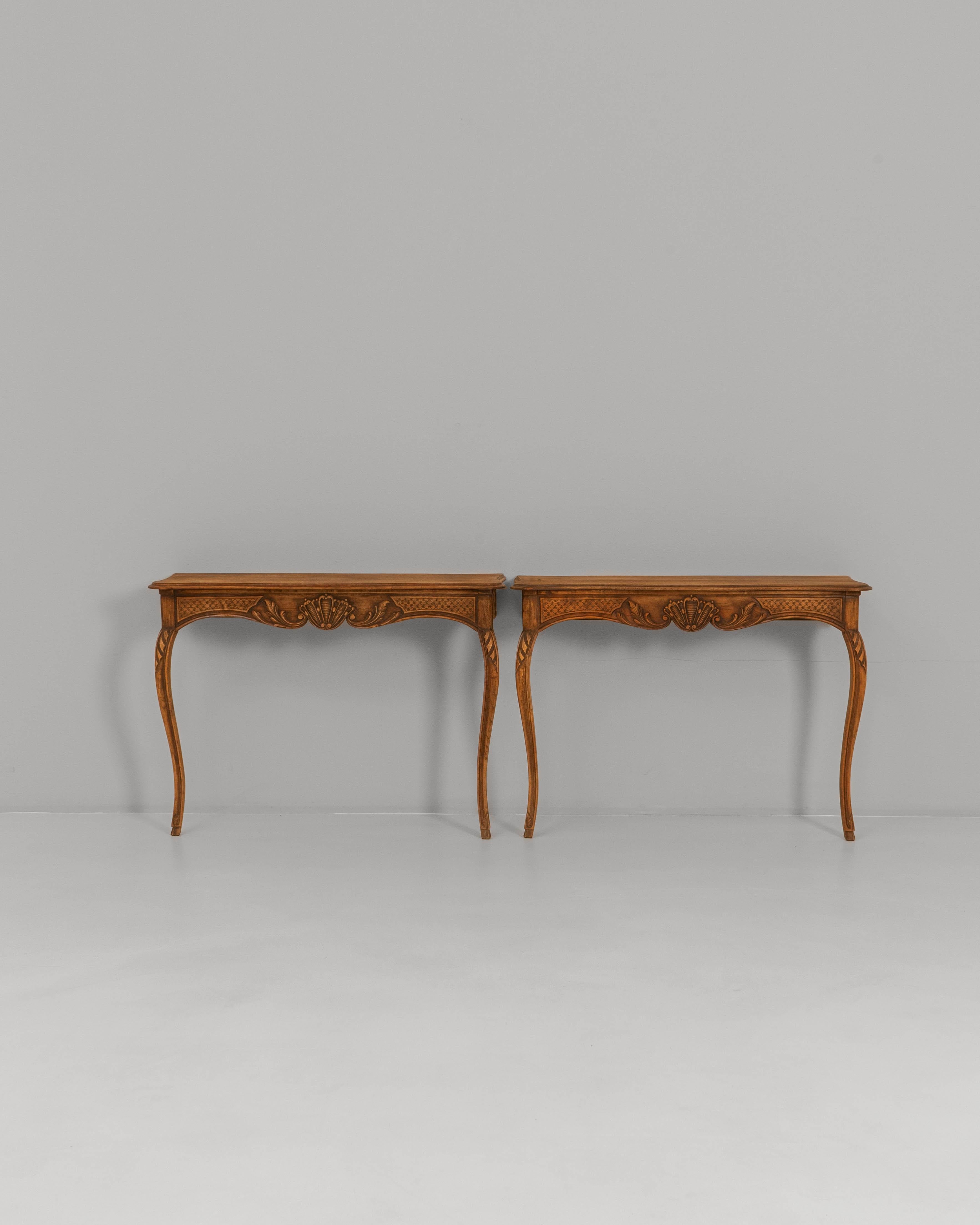 This pair of 19th Century French Louis XV carved wooden console tables showcases the elegance and fluidity characteristic of the period. Each table features a gently curved silhouette supported by cabriole legs adorned with delicate carved details,