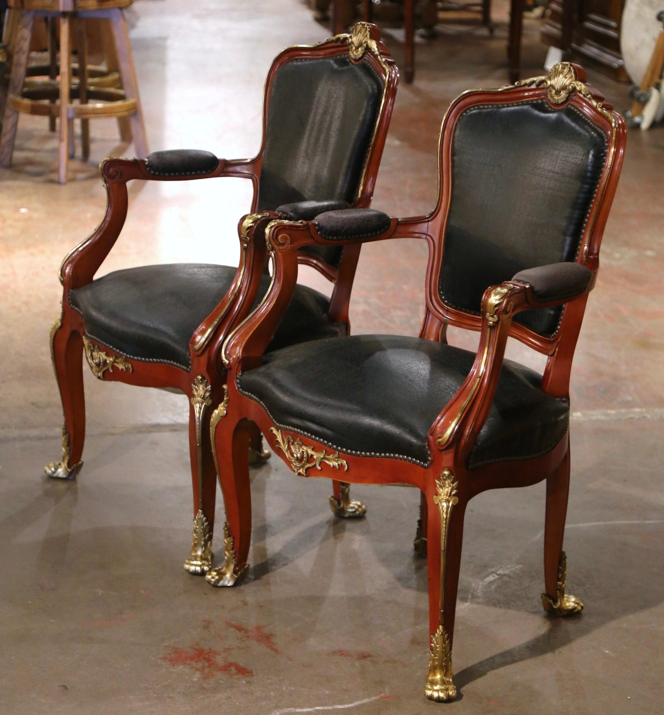 Decorate a study or office with this elegant pair of antique armchairs with gilded ormolu mounts. Crafted in Paris, France circa 1850, and built of mahogany wood, each chair stands on cabriole legs decorated with bronze leaf motifs at the shoulders,