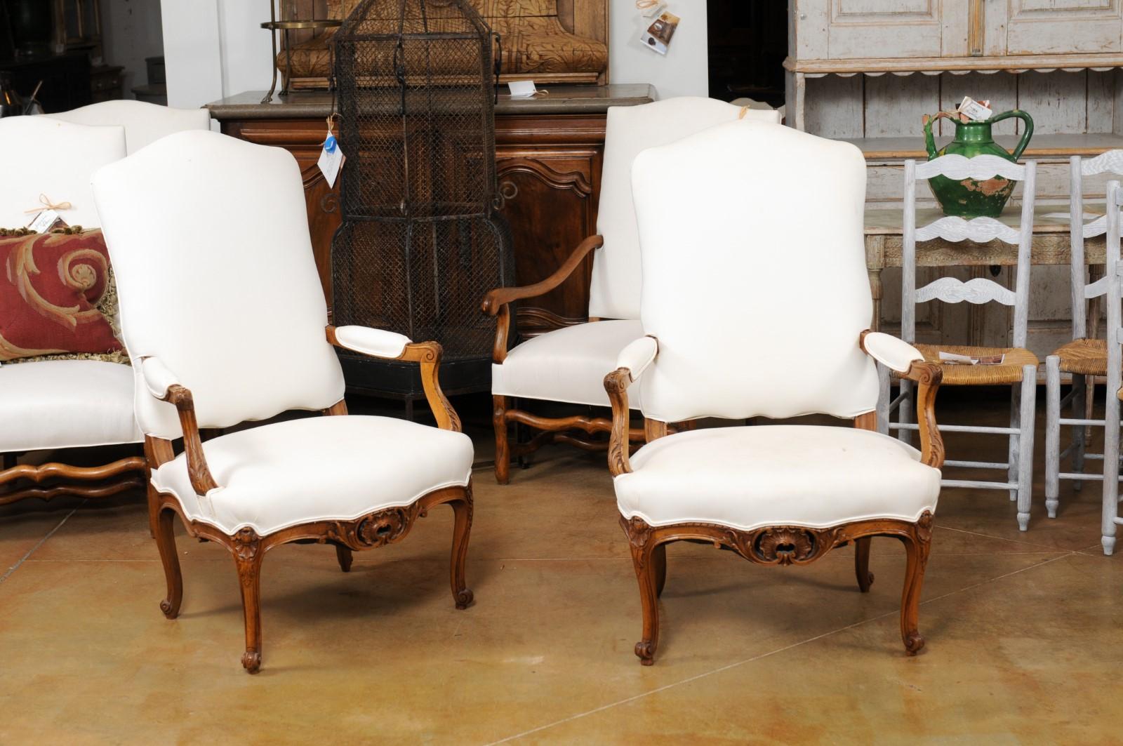 A pair of French Louis XV style walnut armchairs from the 19th century, with carved aprons and upholstery. Created in France during the 19th century, each of this pair of fauteuils features a slanted camelback, connected to two open partially
