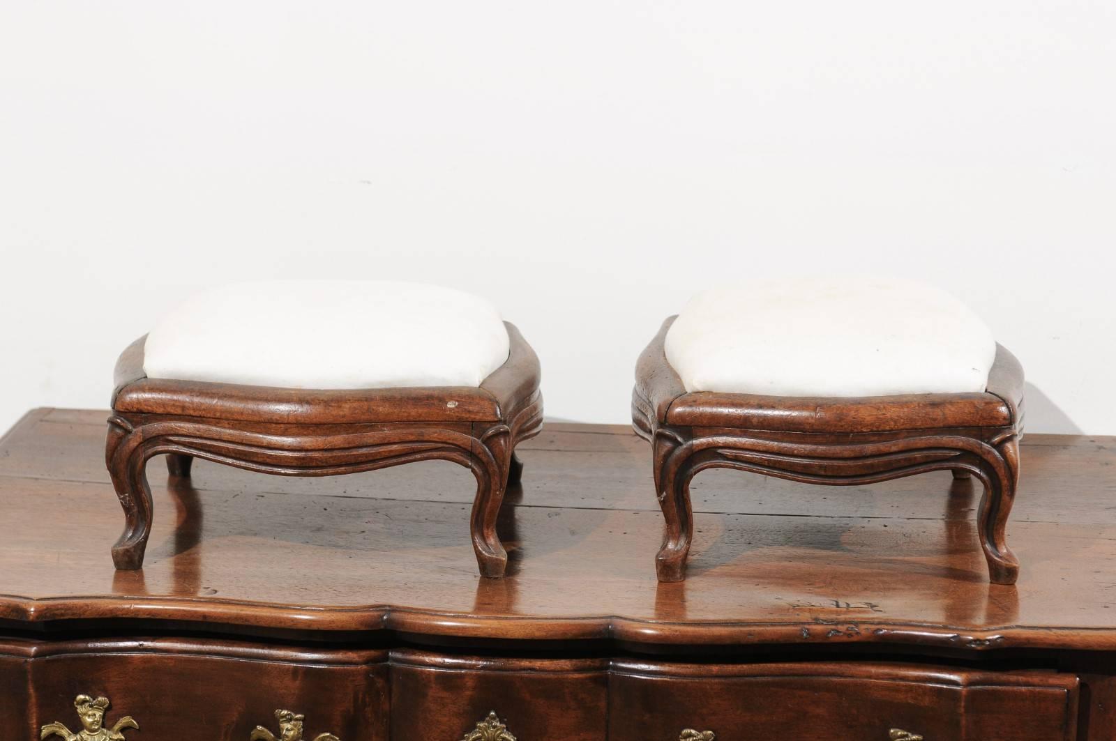 A pair of French Louis XV style walnut footstools from the 19th century with new upholstery. Each of this pair of French stools features a walnut body, carved with delicate sinuous lines. The decor, while understated, is elegant and the stools are