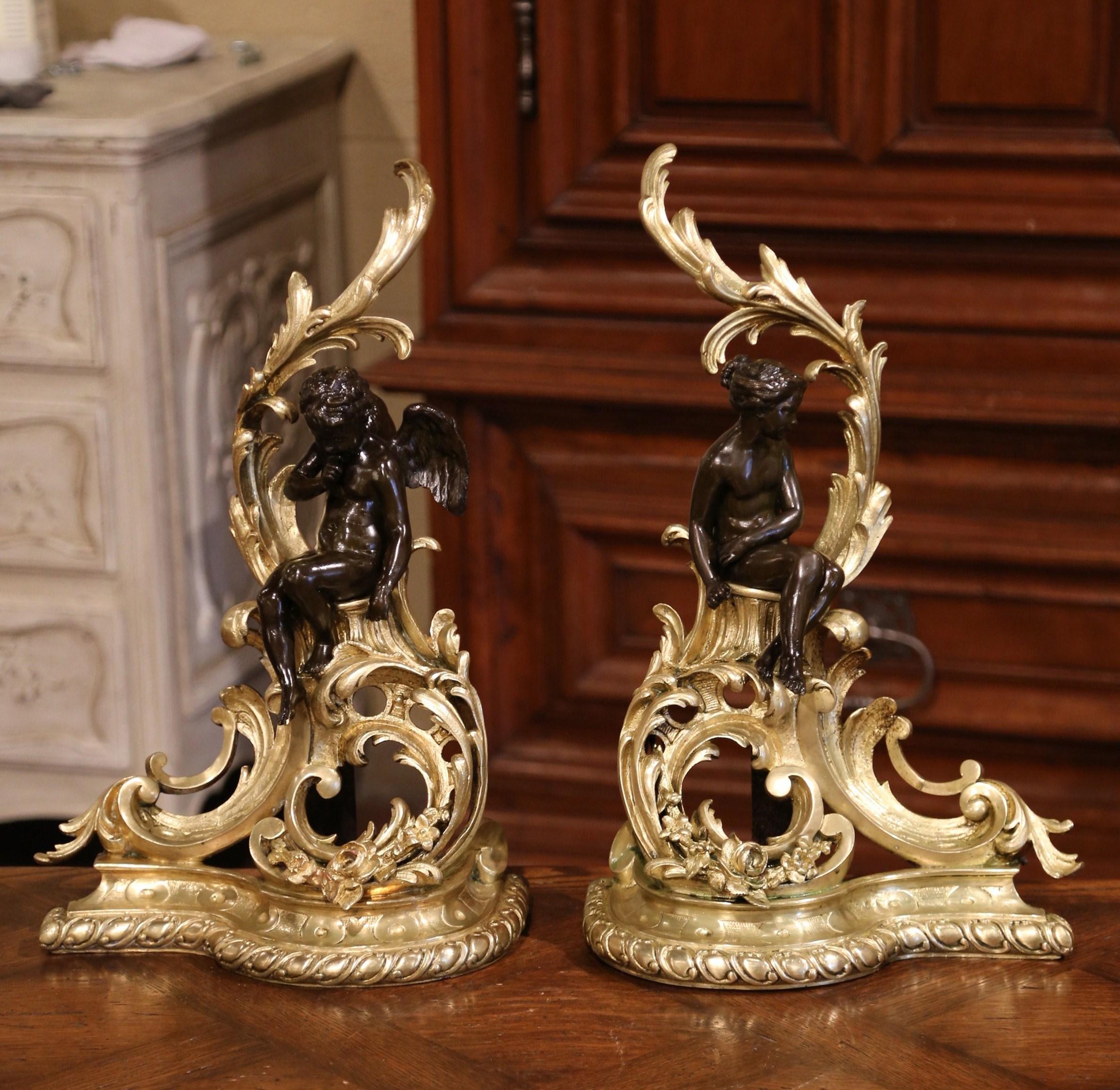 Decorate your fireplace with this elegant pair of antique two-tone bronze chenets. Crafted in France, circa 1860, the sculpted andirons feature intricate foliage and leaf decor embellished with a patinated cherub and female figures, both sited on