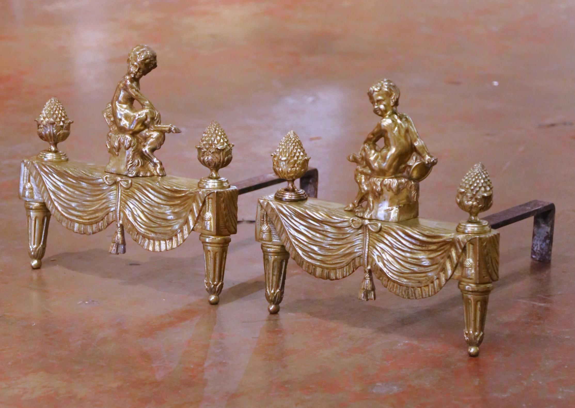 Aporta un refinado encanto neoclásico al hogar con este par de antiguos chenets franceses de estilo Luis XVI, fabricados en Francia hacia 1880 y acabados en cálido bronce dorado. Cada hierro dorado está coronado por un putto sentado finamente