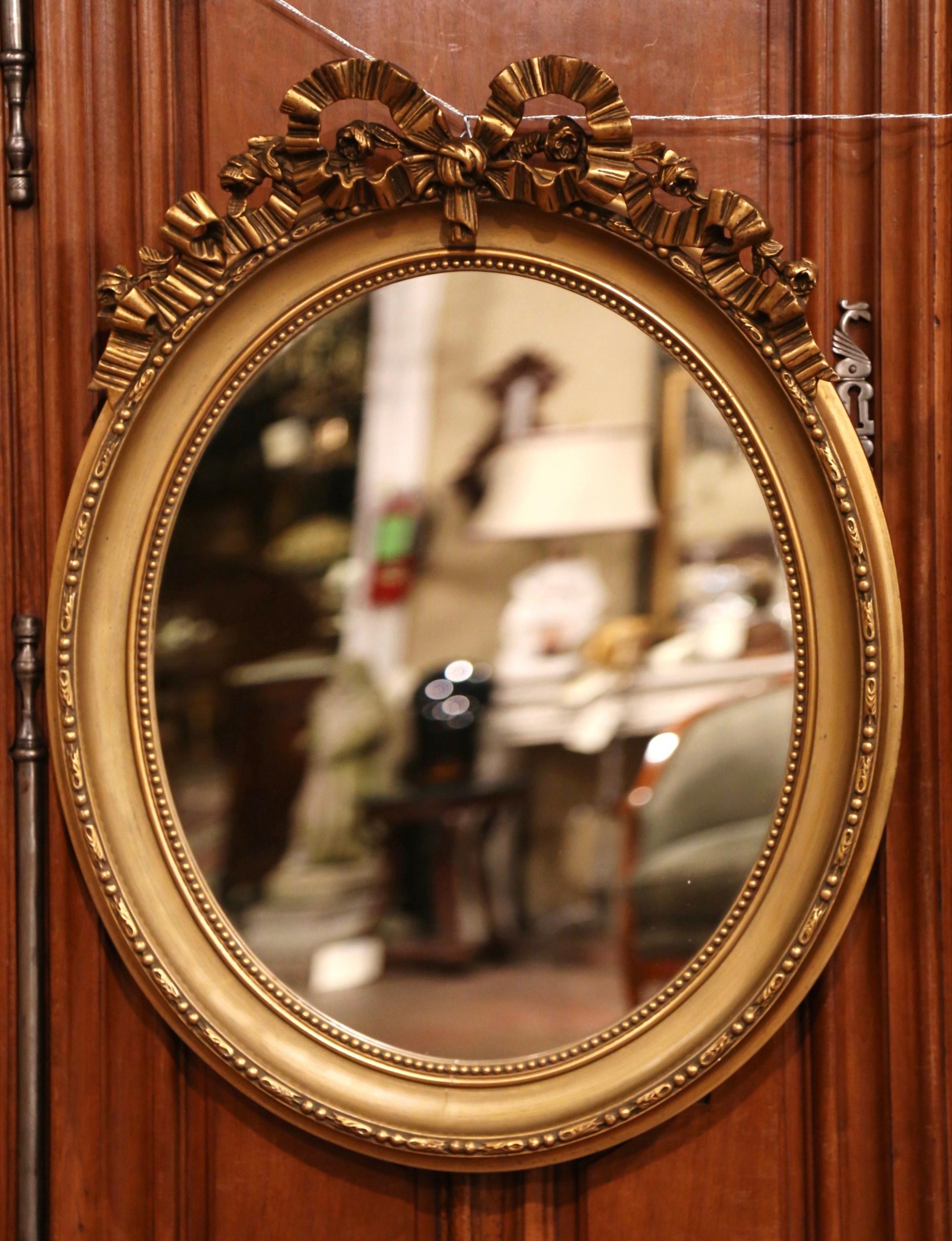 These elegant antique mirrors were crafted in France, circa 1880. Each wall mirror features a traditional carved Louis XVI ribbon bow at the pediment embellished with floral motifs, and the oval frame is decorated with rows of beads around the