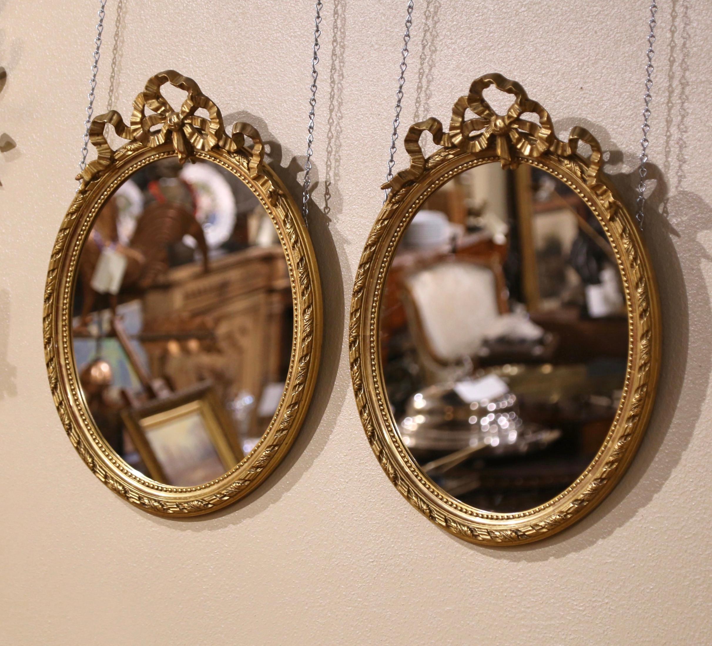 Eleganza per il bagno padronale o per l'ingresso con questa elegante coppia di antichi specchi da parete. Realizzato in Francia intorno al 1880 e di forma ovale, ogni specchio è decorato con il tradizionale fiocco Luigi XVI sul frontone e