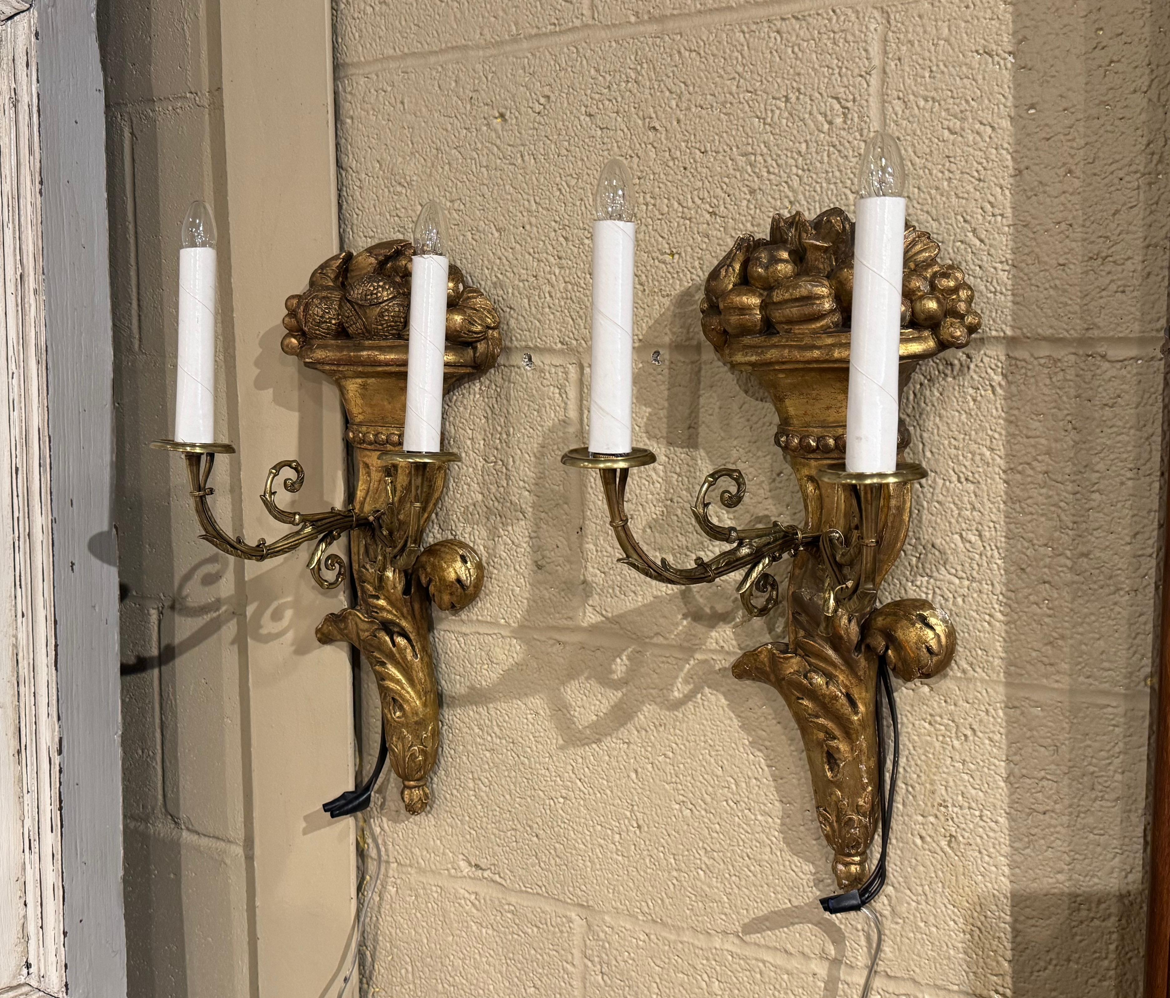 Decorate a wall with this elegant pair of antique carved gilt sconces. Crafted in France, circa 1870, each sconce is embellished with a hand carved assorted fruit and nut basket at the pediment, and ending with acanthus leaf motifs at the bottom.