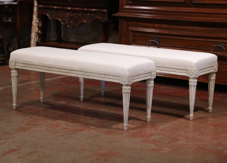 Complete your entryway or living room with this pair of antique benches from France, circa 1890. Rectangular in shape, these pieces sit on four tapered and fluted legs decorated with carved floral medallions at each corner, and feature an intricate