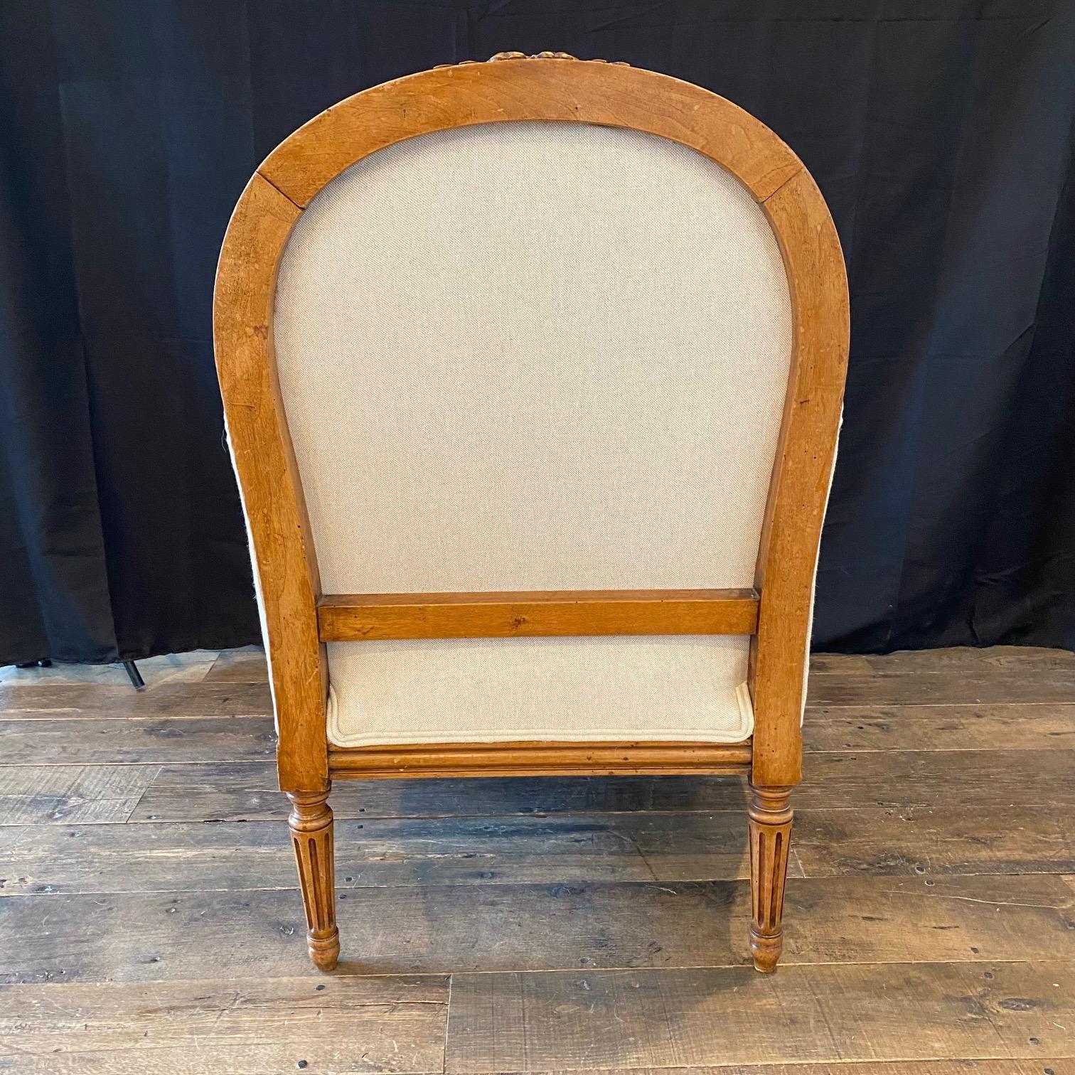 A pair of timeless and elegant French Louis XVI armchairs from the 19th century having a shapely, upholstered back, with  arched crest rail, all framed within molded wood trim. Carved wood arms, with manchette pads for comfort, terminate into