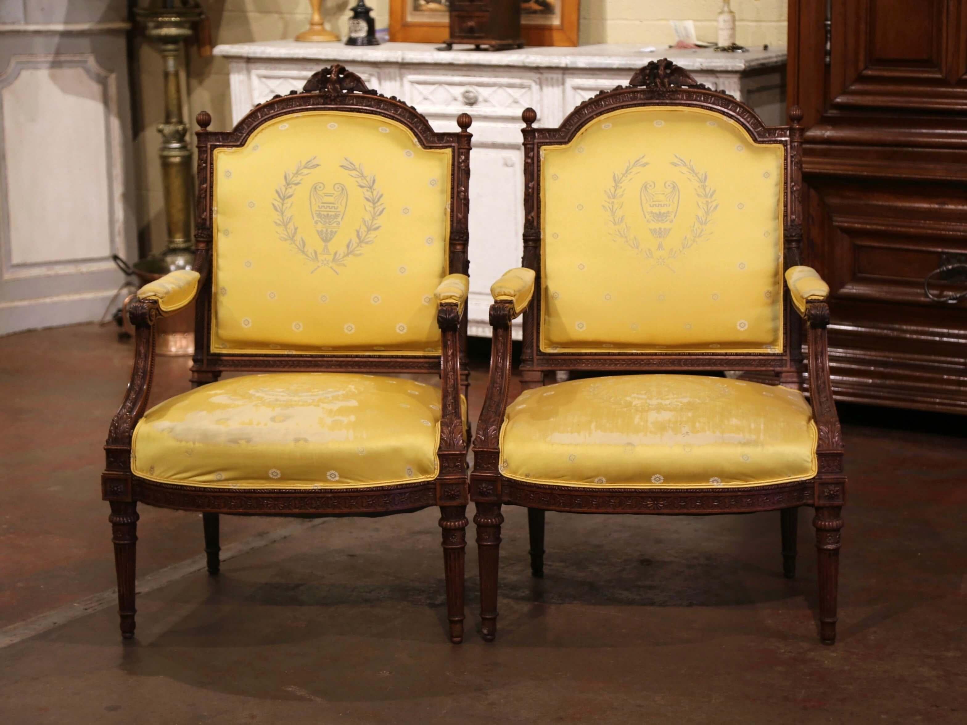 Complete your formal living room or den with this elegant pair of antique armchairs. Created in France, circa 1880, the large, classic bergeres stand on carved tapered and fluted legs over a bombe apron. Each wide and rounded back is decorated with