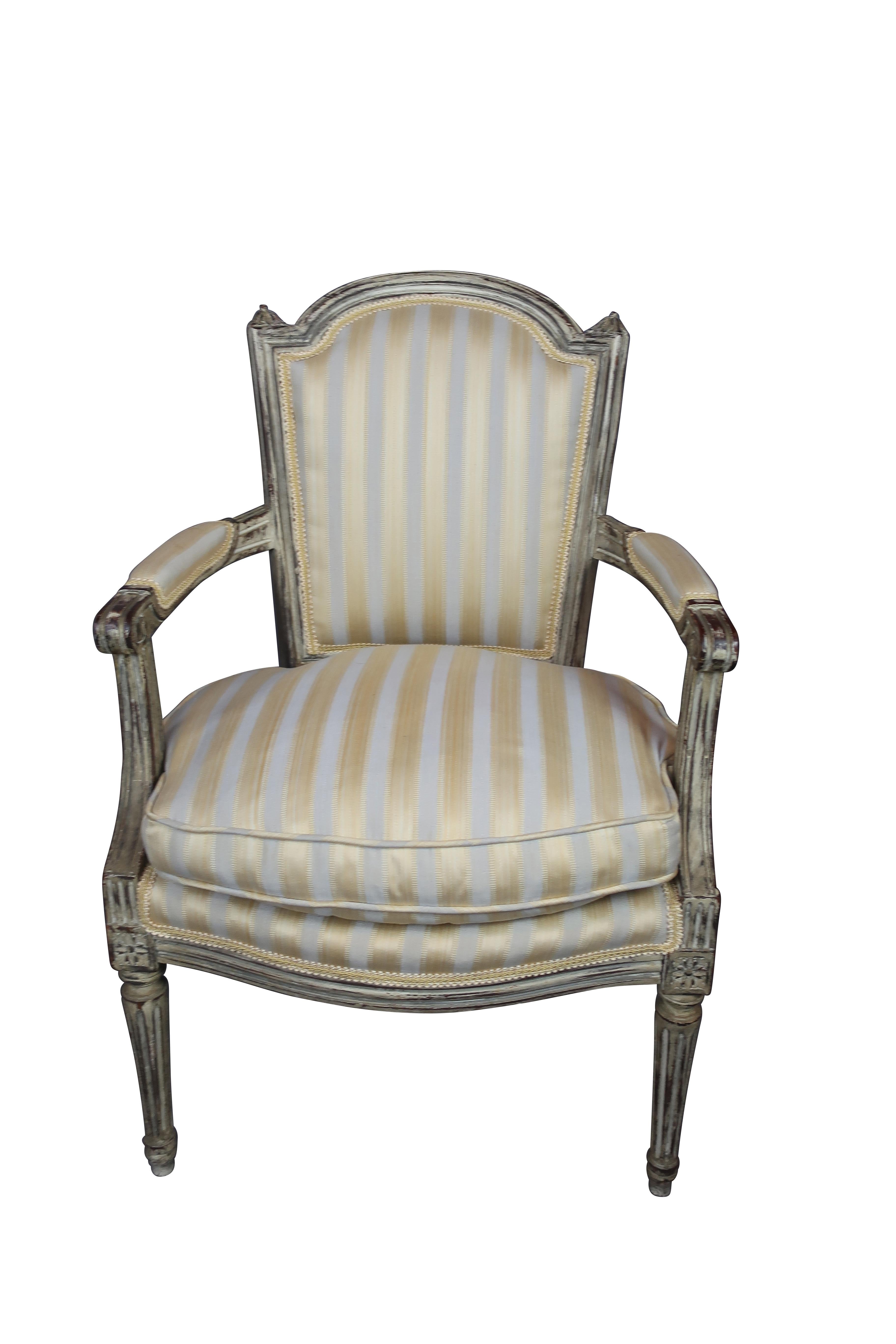 Pair of 19th century French Louis XVI grey painted upholstered chairs, frames with gray paint and gold and grey striped upholstery, padded armrests on carved supports, raised on tapered stop fluted legs, carving in the manner of Jean Baptiste