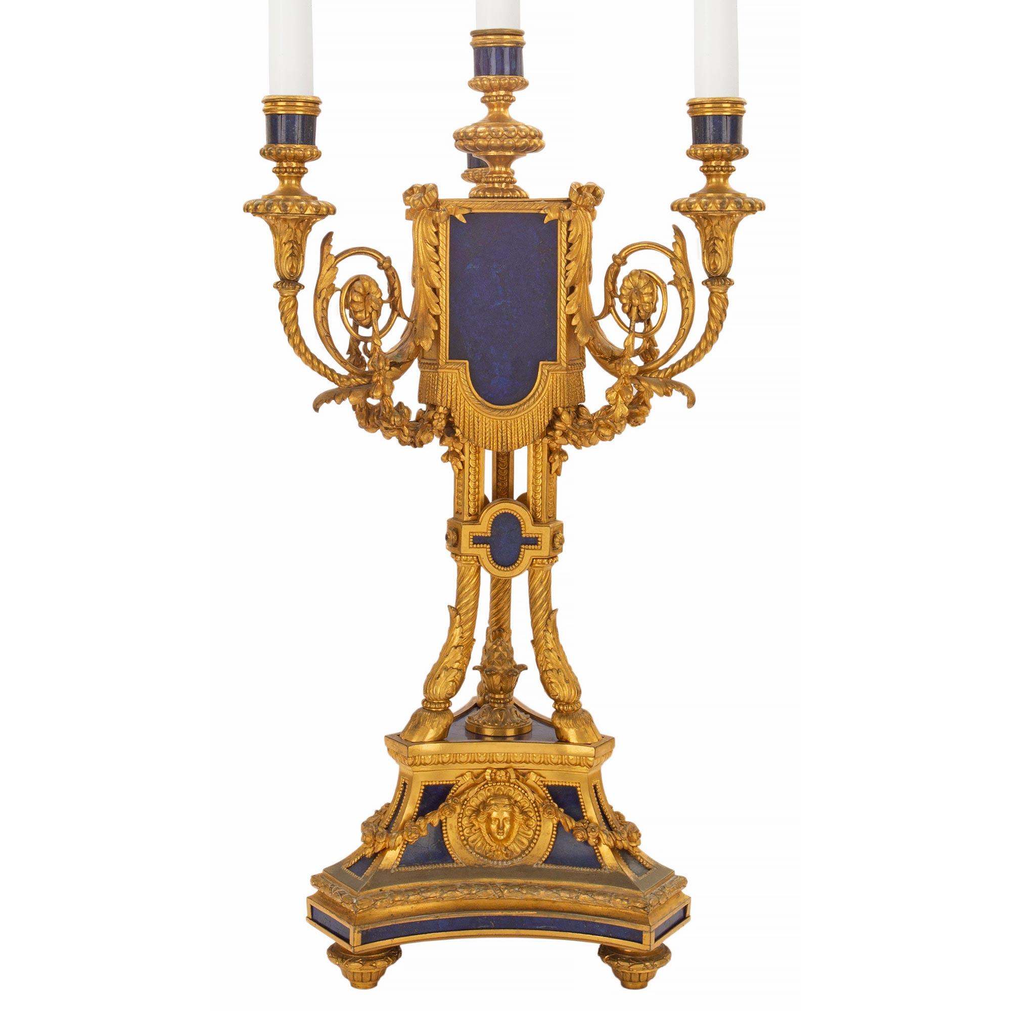 A spectacular and large-scaled pair of early 19th century French Louis XVI st. ormolu and Lapis Lazuli four arm candelabras. The pair with all original gilt is raised by a triangular base with floral garlands and a central medallion of the sun king.