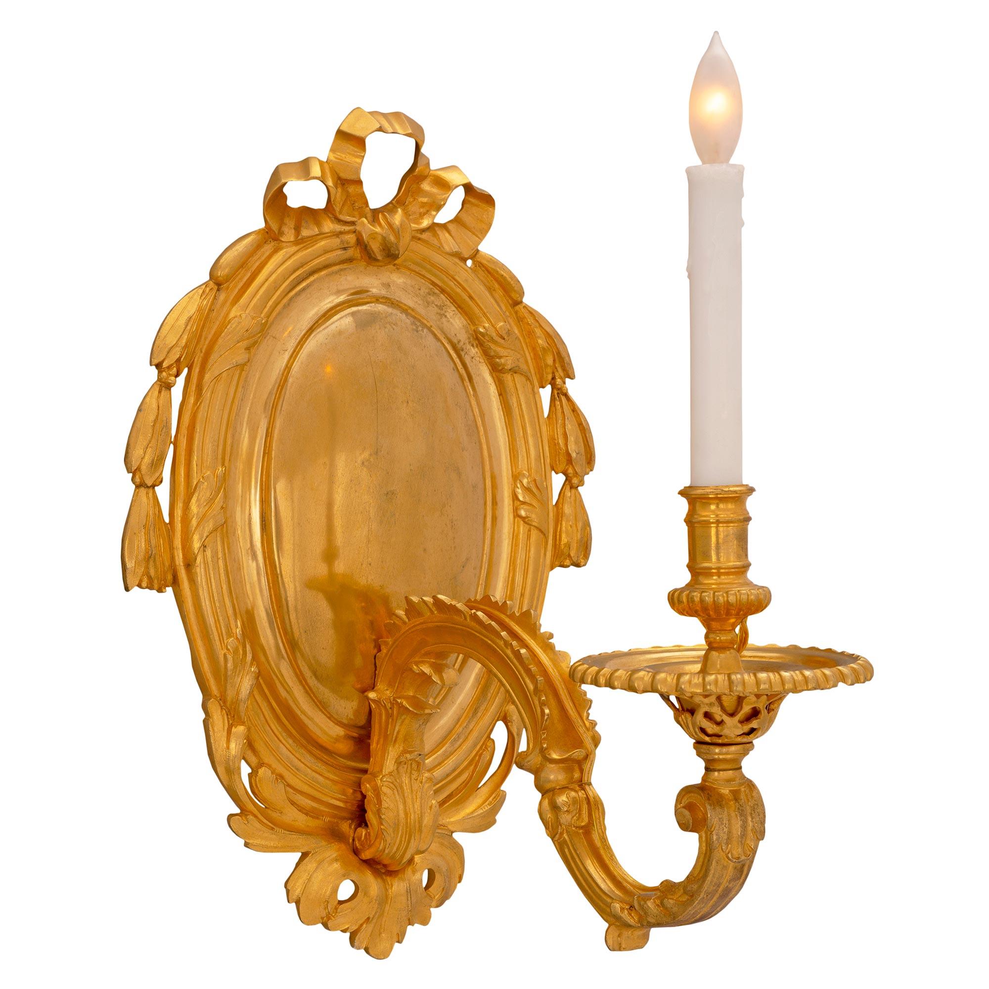 A most attractive pair of French 19th century Louis XVI st. ormolu sconces. Each sconce displays an oval backplate, decorated laurel garlands centered by a bow at the top, and pierced acanthus leaves at the base. Each of the scrolled acanthus leaf