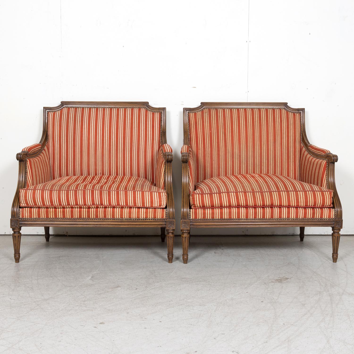 A fine pair of carved 19th century French Louis XVI style bergère marquise upholstered armchairs, often referred to as ‘The Queens’ chair, having walnut frames with neoclassical carved details, circa 1880s. Each oversized chair features a low