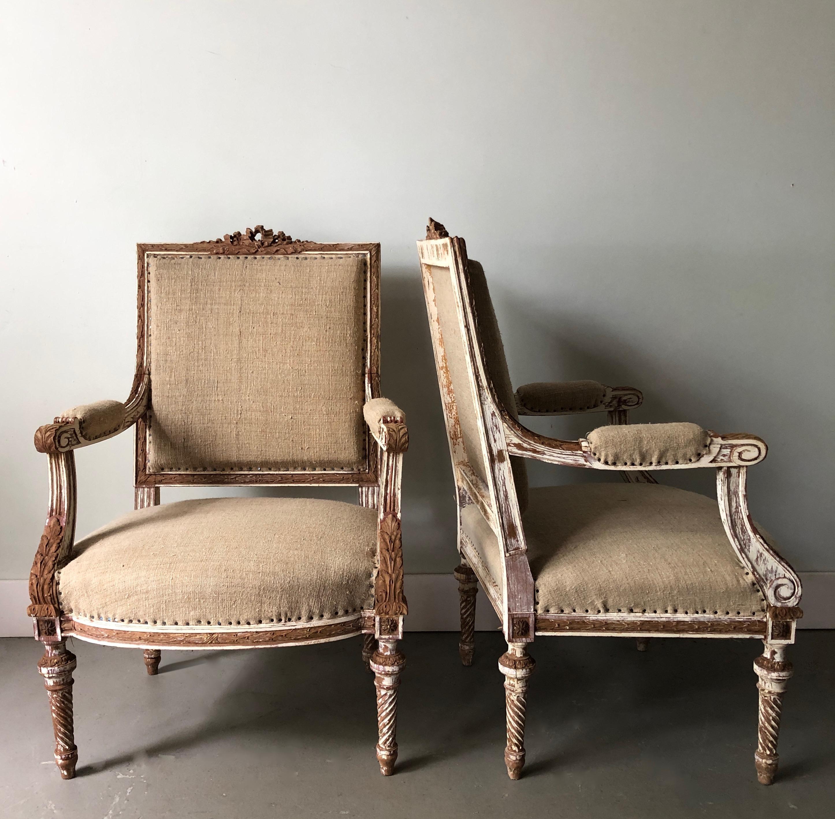 A pair of 19th century French armchairs à la reine with flat back and richly carved solid wood frame with ribbons, acanthus and rosettes on conical twisted fluted legs, showing some places fragments of original giltwood.
Upholstered in raw