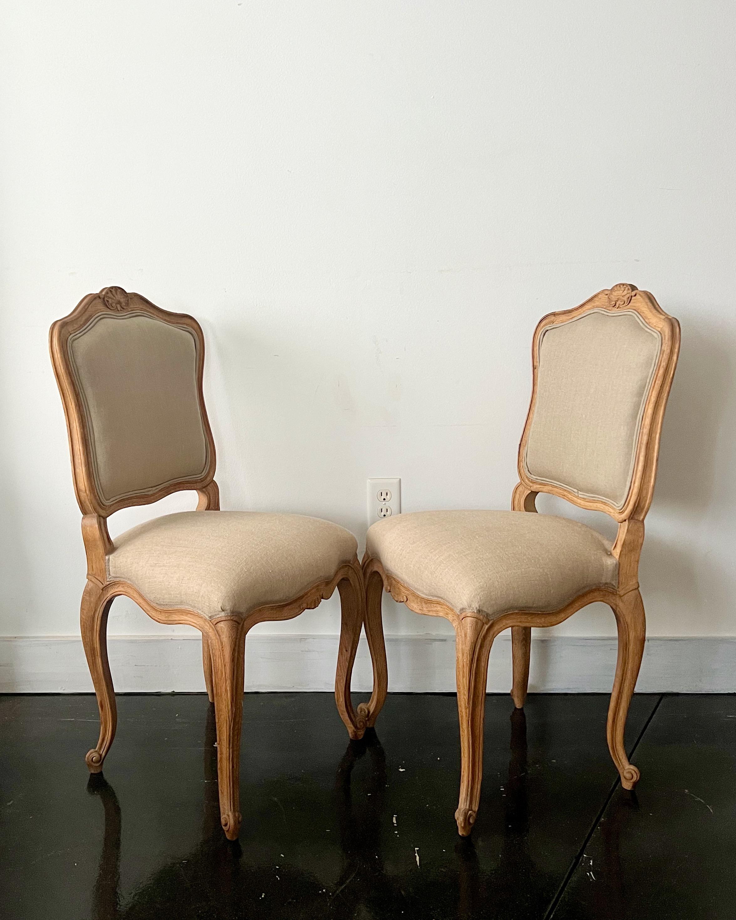 Set of two in natural oak French chairs in Louis XV style with flat back called “la Reine”, scalloped frieze and carved, raised on cabriole legs. 
Upholstered in natural linen. Very elegant as well as comfortable, 
France, circa 1880.
NOTE:
The back