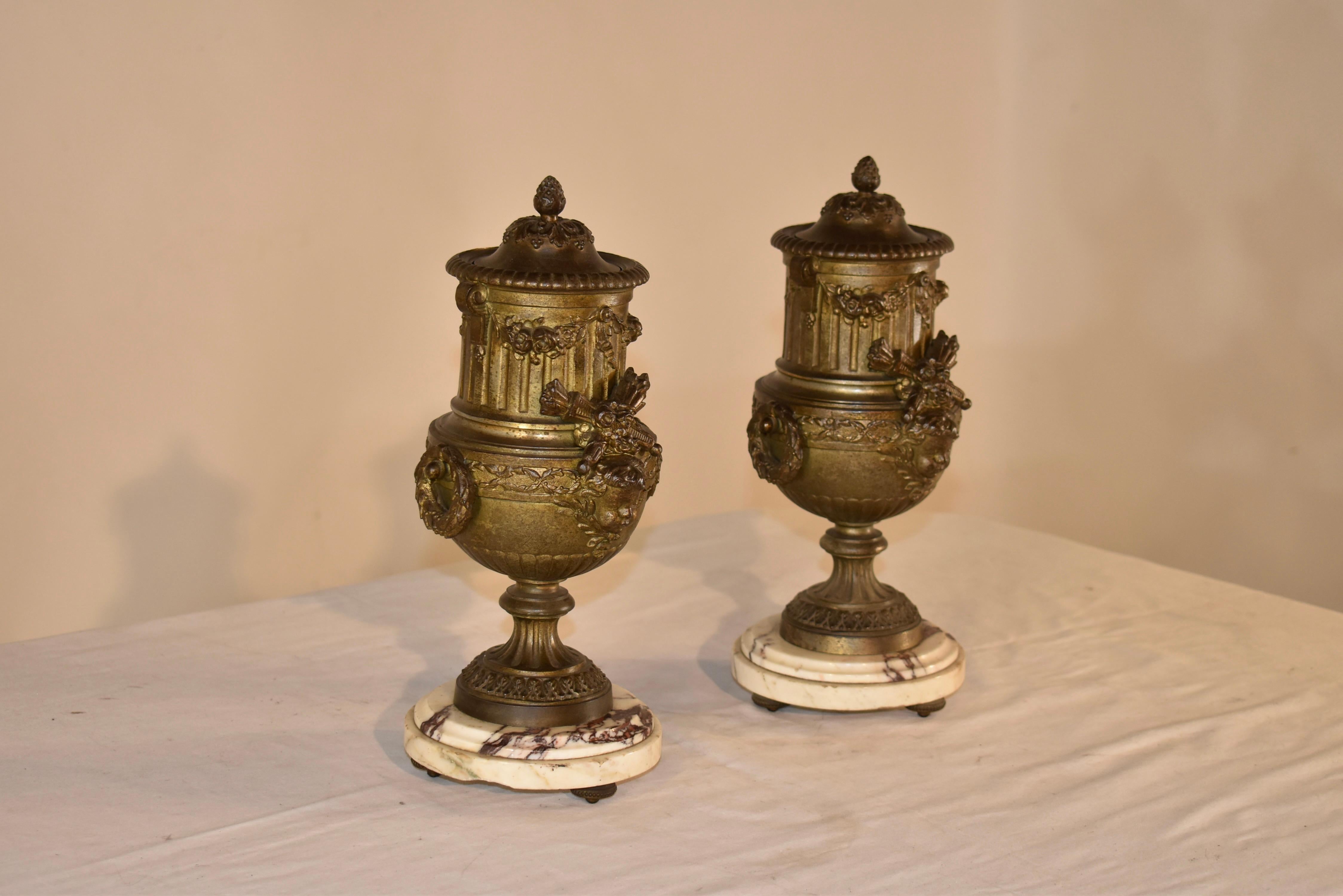 Pareja de urnas de manto del siglo XIX procedentes de Francia.  La pareja tiene tapa y está maravillosamente moldeada con guirnaldas, diseño de cañas y manojos cruzados de lo que parece ser trigo o cosecha de algún tipo adornado con caras.  Las