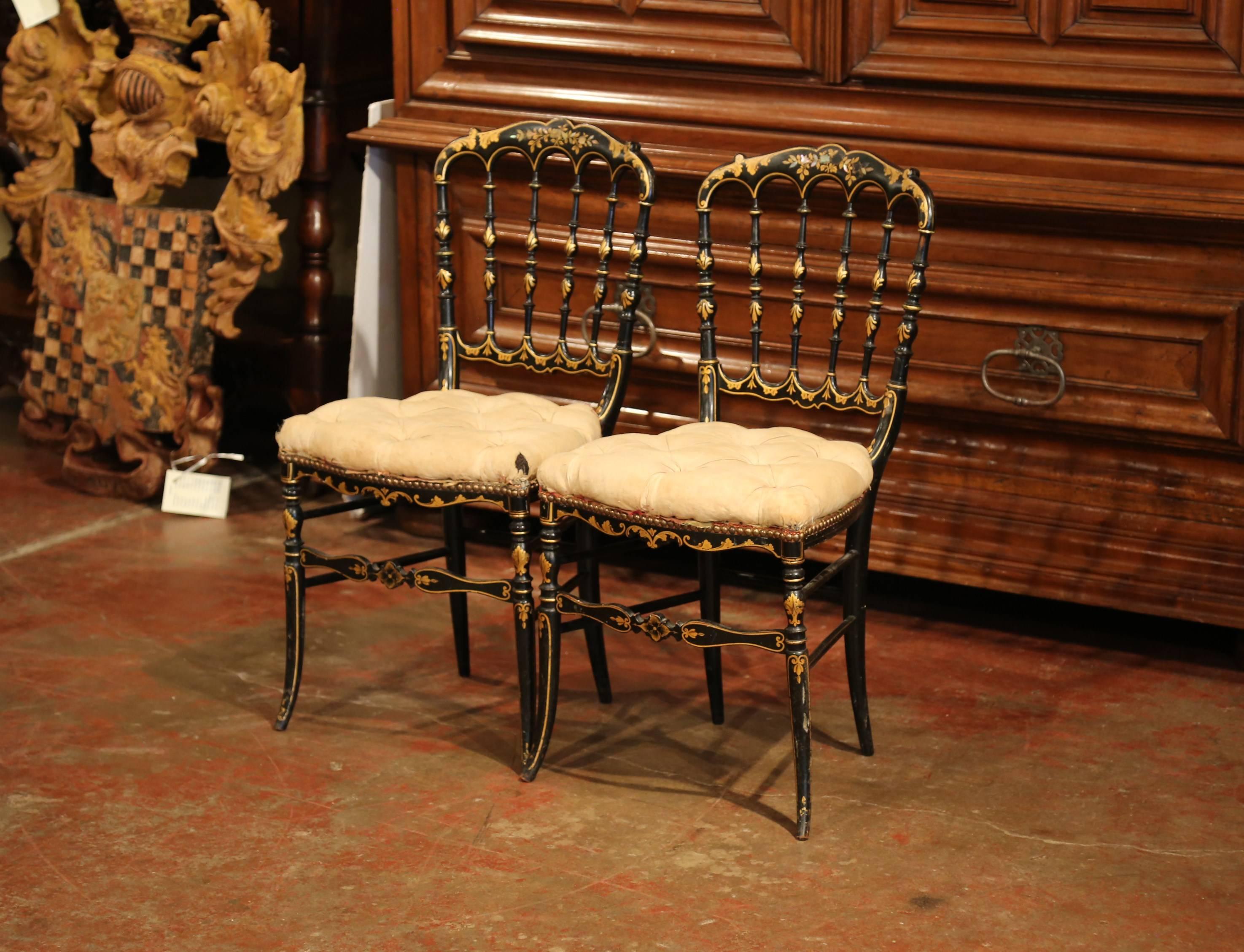 This elegant pair of chairs was created in France, circa 1870. Each antique petite chair frame features a ladder back with spindles, four curved legs and a front shaped apron. The chairs have a shiny, black lacquered paint finish and are embellished