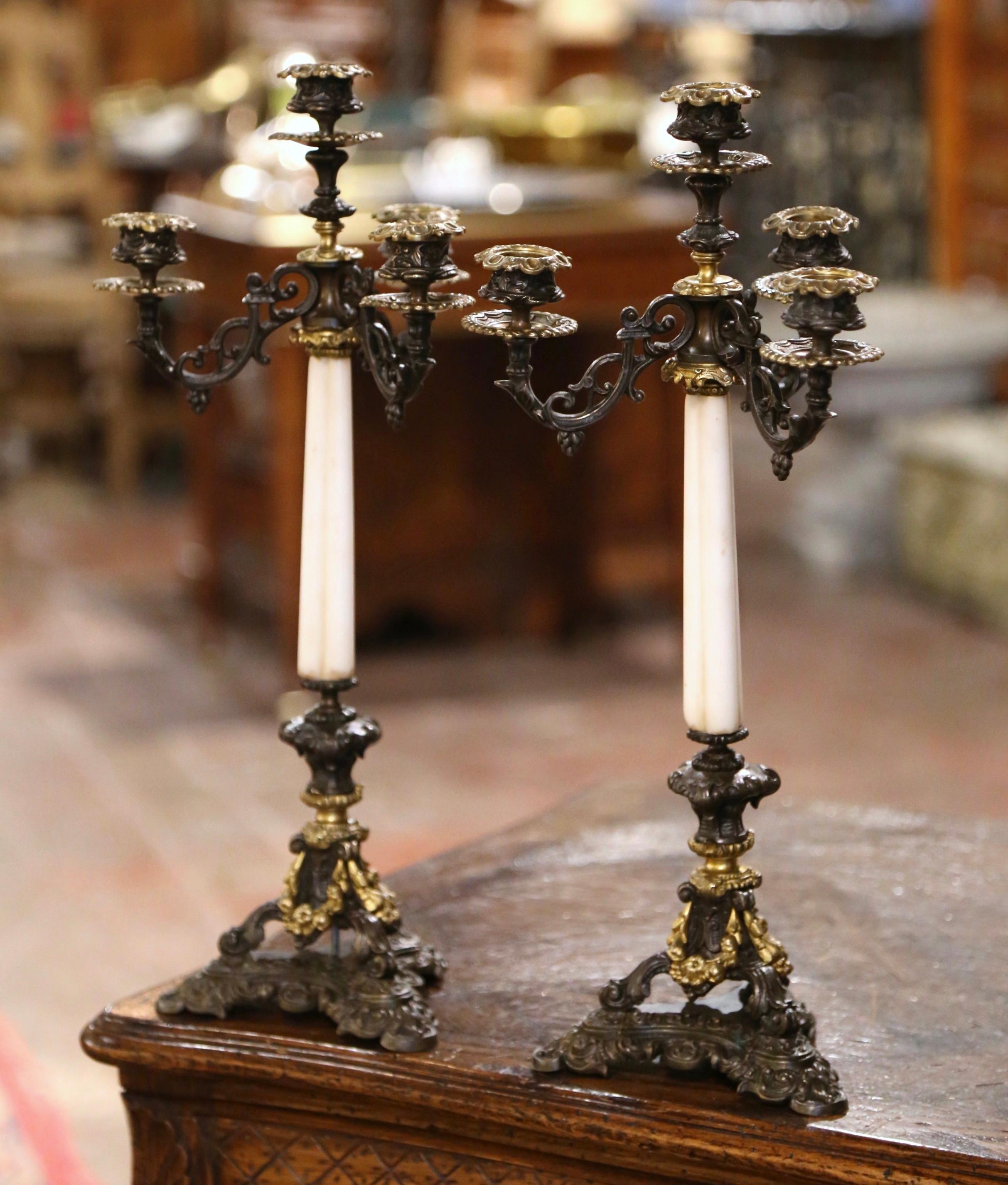 Decora una console o un caminetto con questa elegante coppia di candelieri antichi. Realizzato in Francia intorno al 1870, ogni candelabro poggia su tre piedi a voluta su una base a treppiede integrale. L'intricata base è decorata con decorazioni di