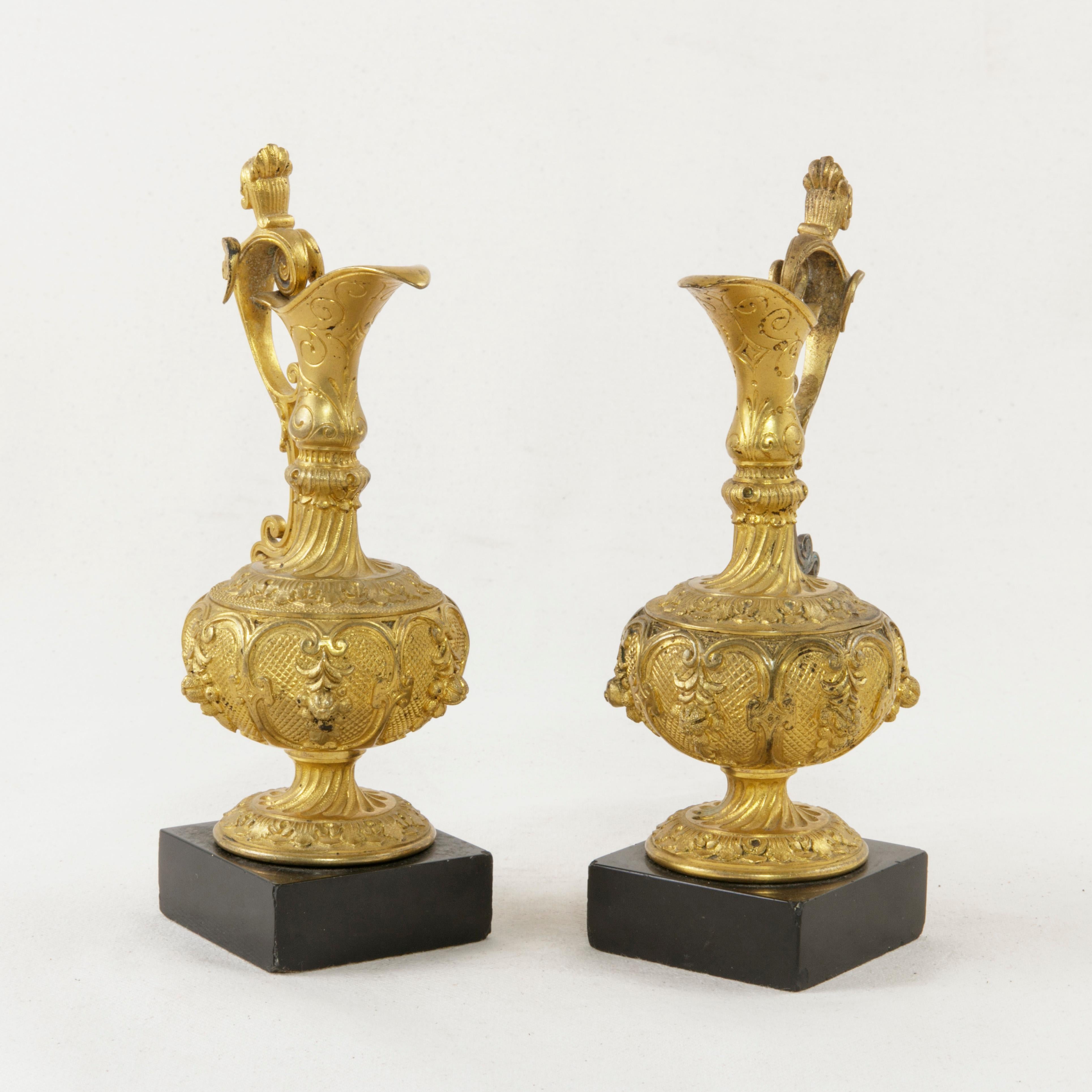 This pair of mid-19th century French Napoleon III period gilt bronze cruets features elegant detailing of leaves and winged female busts on the scrolling handles. A long spout is finished with incised scrolling. Each cruet rests on a 2.25 inch