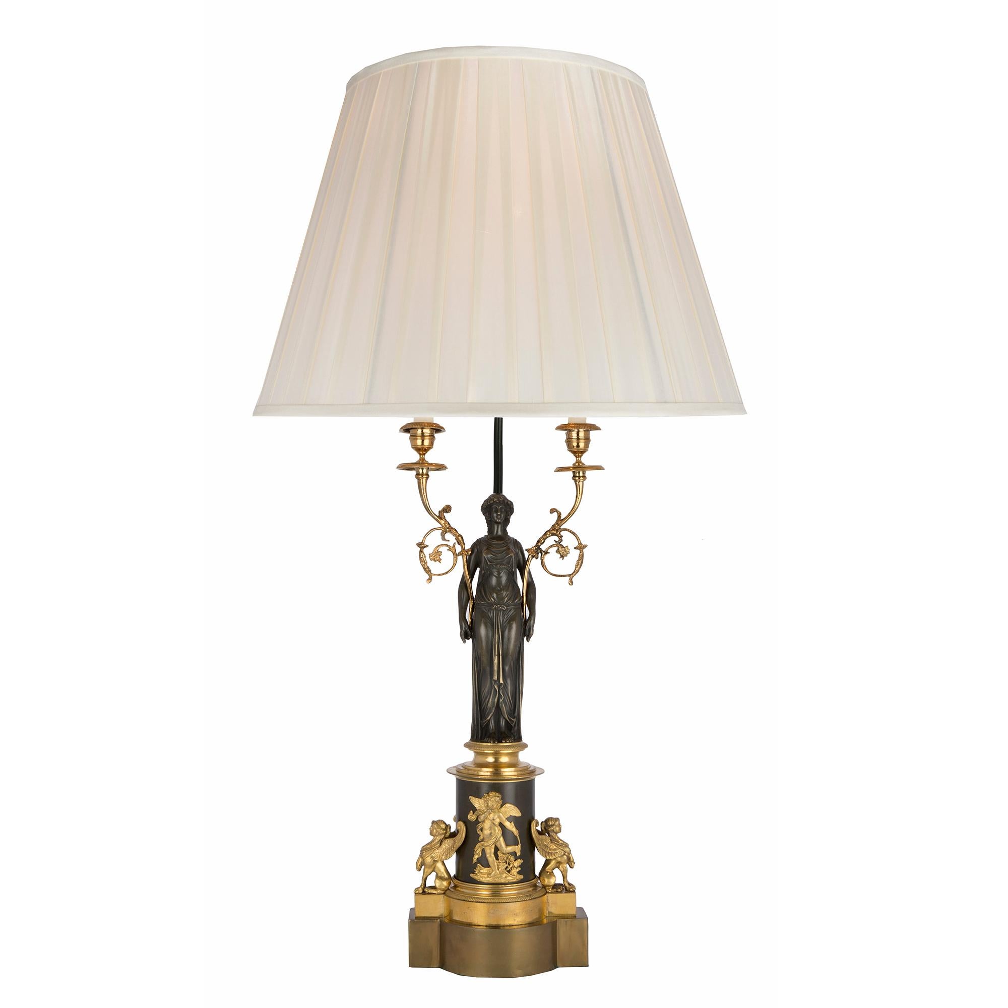 Une jolie paire de candélabres néo-classiques français du 19e siècle en bronze patiné et bronze doré, montés en lampes. Chaque lampe avec une base en bronze doré soutient le piédestal en bronze patiné qui est flanqué d'une paire de griffons ailés en