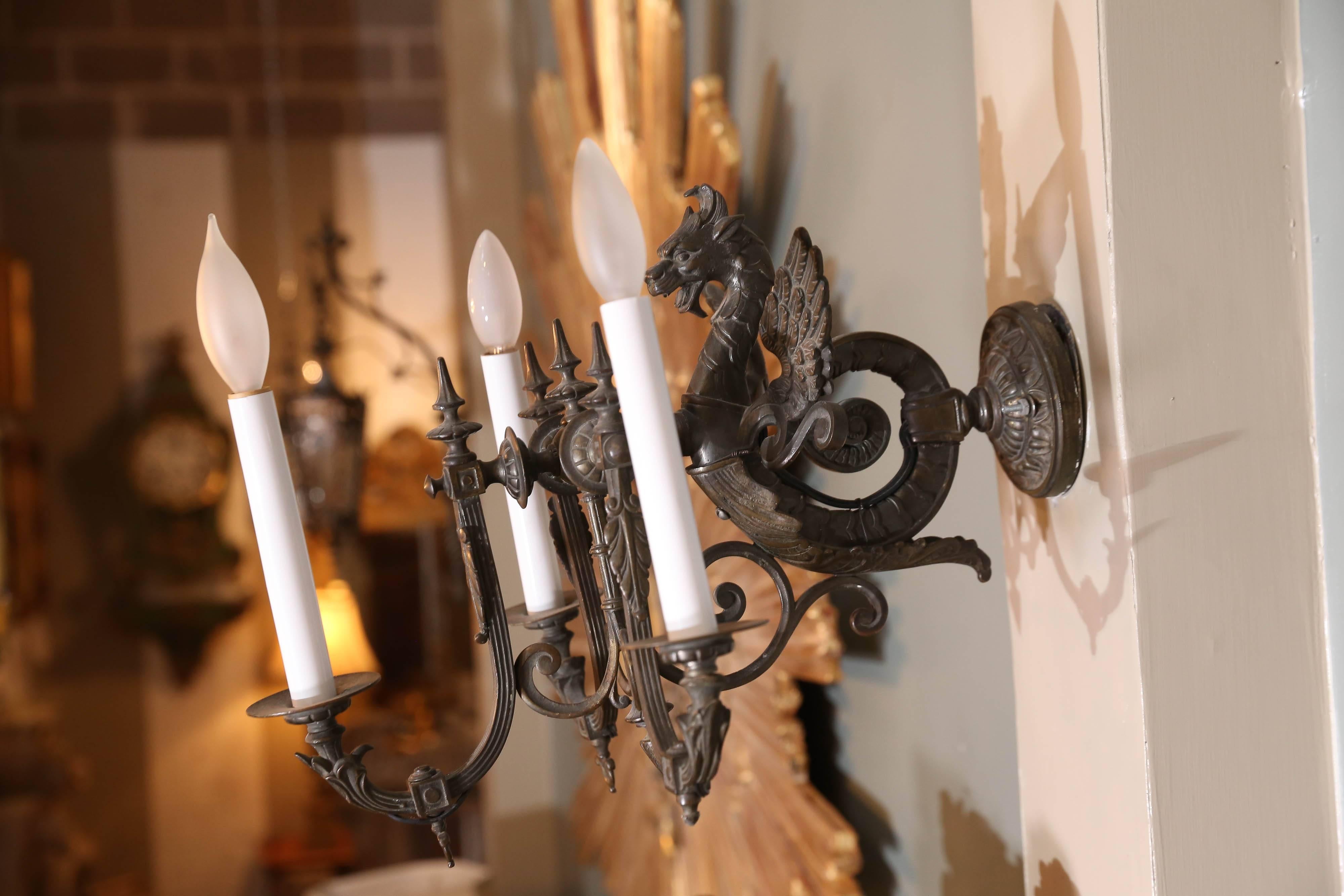 Dramatic pair of French neoclassical bronze three-lite Griffon sconces are finely detailed, including the wall mount canopy.
Fierce looking Griffon boasts wings and a tail that curls and is attached to canopy. An acanthus leaf attaches to