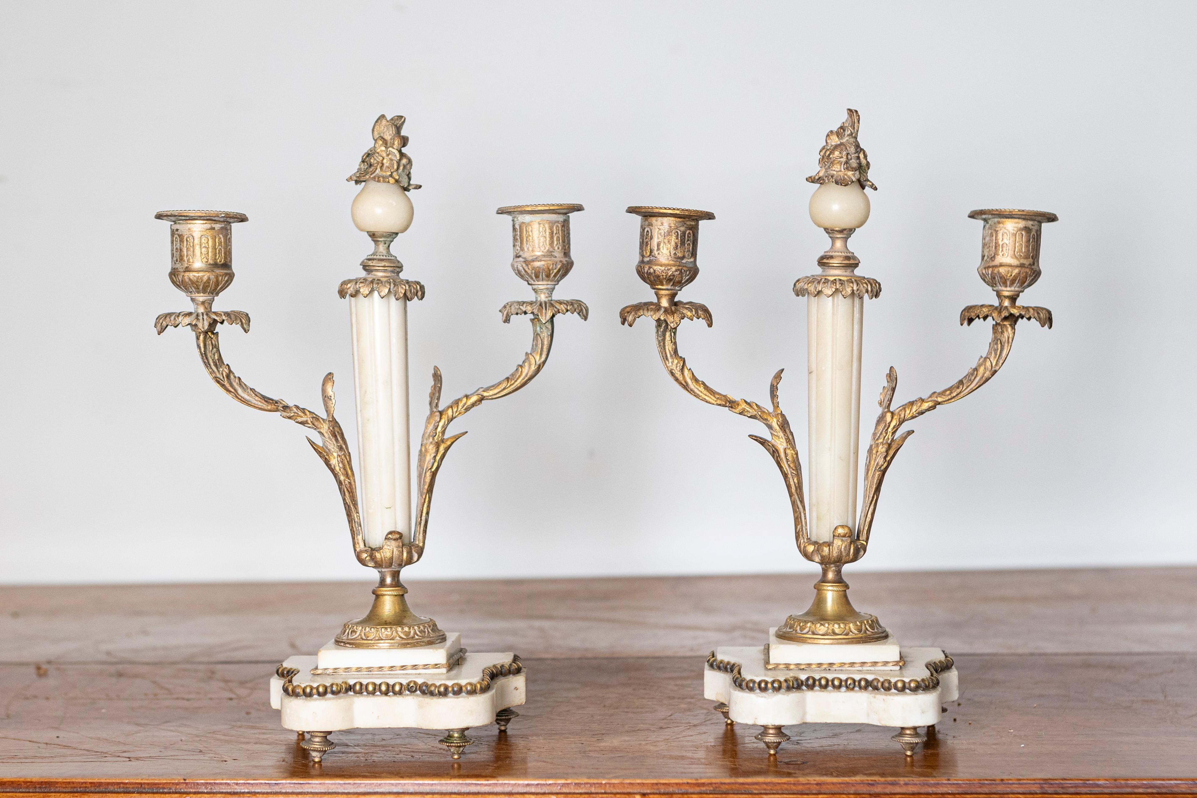 Questa elegante coppia di candelieri francesi del XIX secolo esemplifica lo stile neoclassico, con colonne di marmo bianco ornate da montature in bronzo dorato e dettagli intricati. Ogni candelabro contiene due bracci di candela, che si estendono