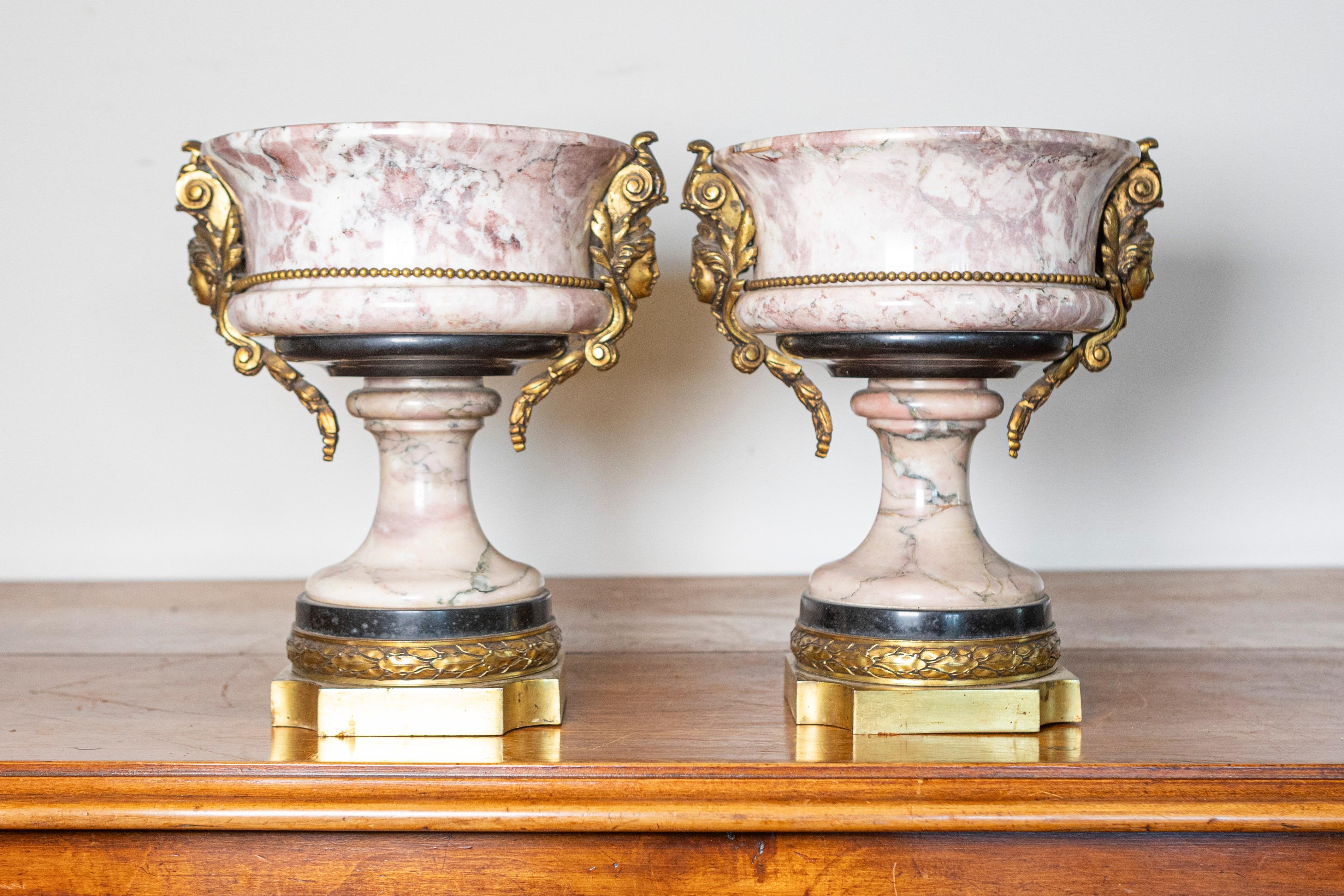 Questa squisita coppia di urne francesi del XIX secolo mostra l'eleganza e la maestria del periodo neoclassico, con marmo rosa venato finemente intagliato e completato da montature in bronzo dorato o ormolu. Le urne poggiano su basi quadrate in
