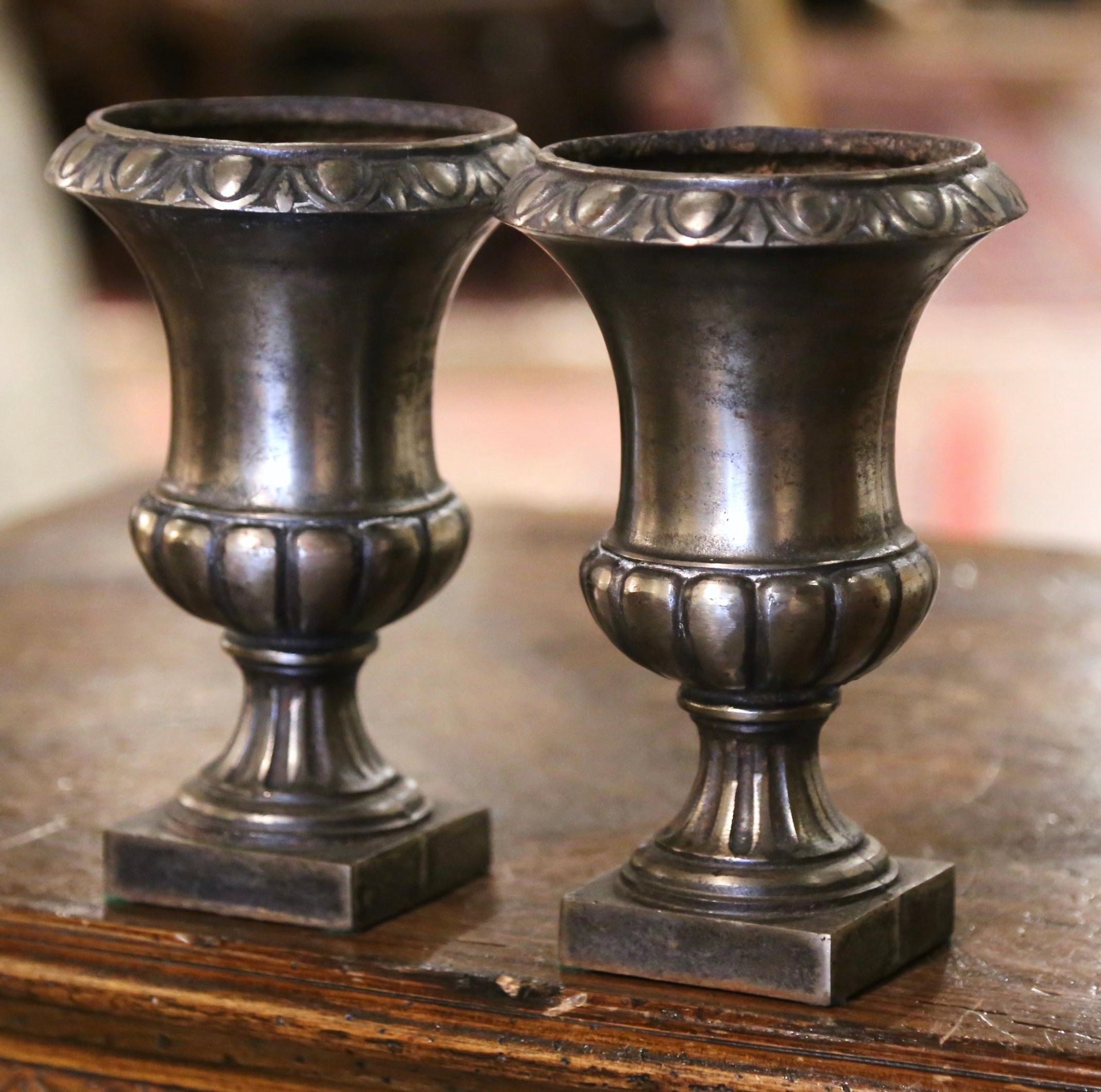 Decorate a mantel or buffet with this elegant pair of classical Roman antique urns. Crafted in France circa 1870, each vase stands on an integral platform square base, over a gadrooned body ending with a wide mouth with flared rim and molded trim at