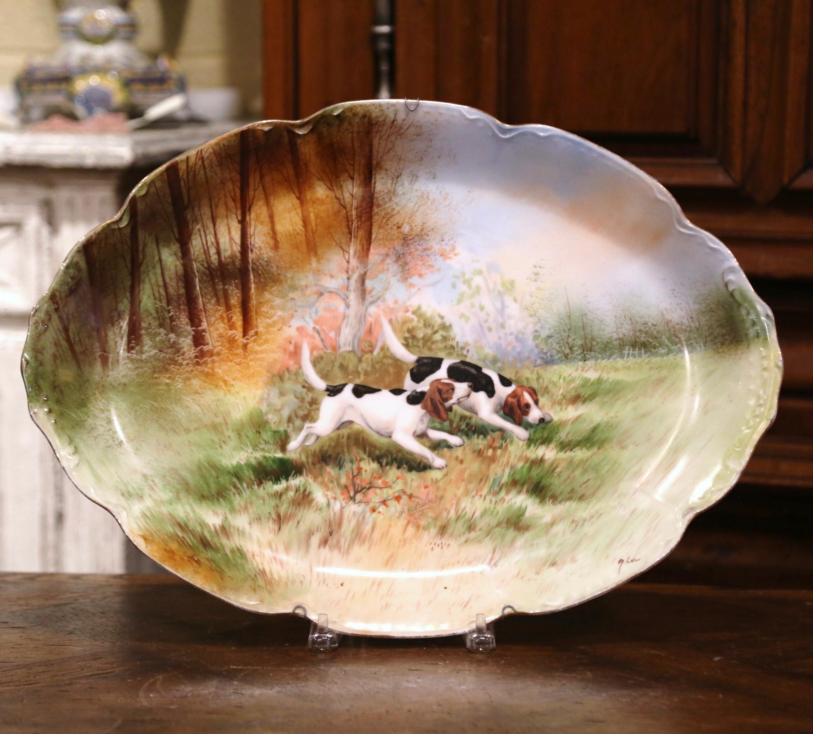 Decorate a wall or a shelf with this colorful pair of antique wall platters. Crafted in Paris France circa 1870 and signed, each hand painted porcelain plate is oval in shape with a scalloped rim, and features a pastoral scene with hunting dogs in
