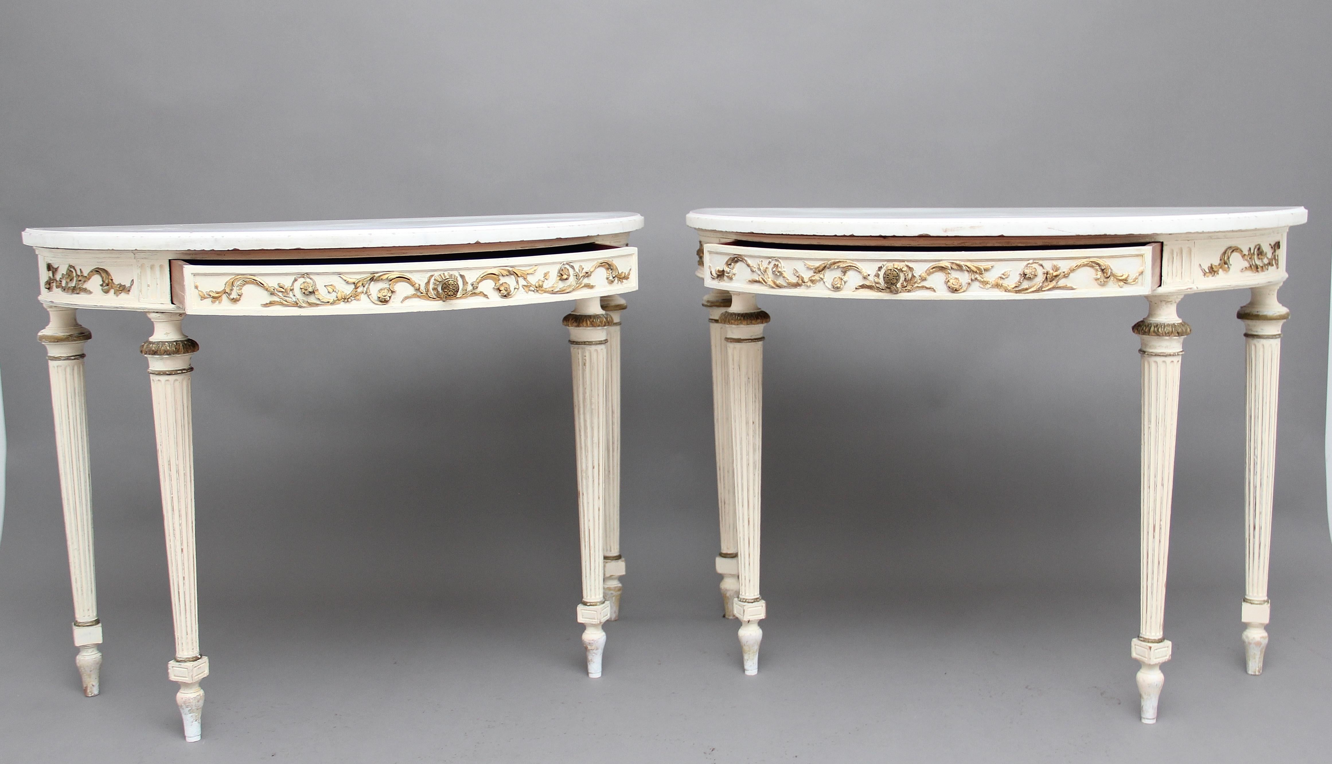 A decorative pair of 19th century French painted console tables, having the original white marble tops above a frieze with raised gilt decoration, a mahogany lined drawer at the centre with original engraved turned handle, supported on turned and